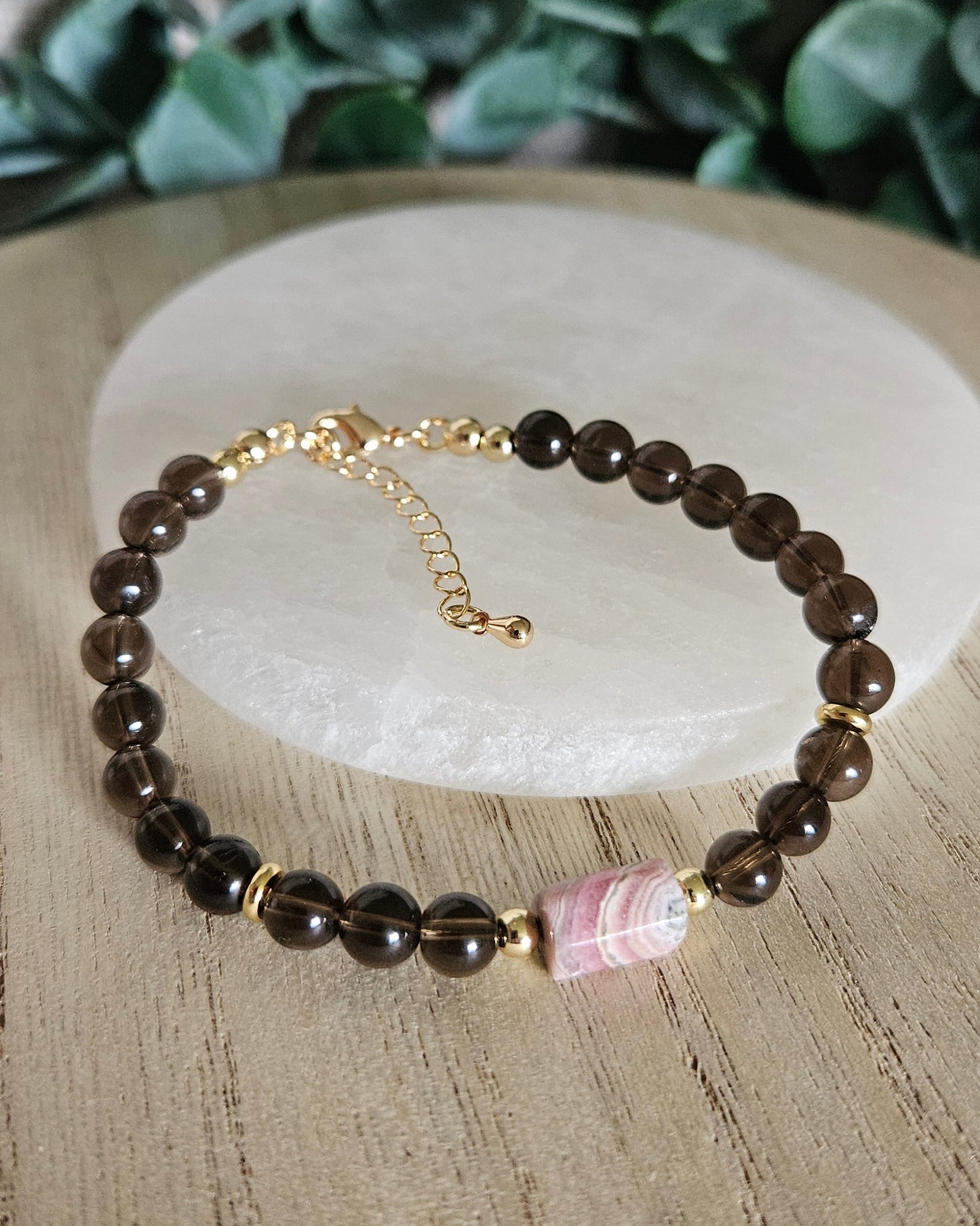 Smoky Quartz and Rhodochrosite bracelet arranged before a round selenite plate with eucalyptus in the background