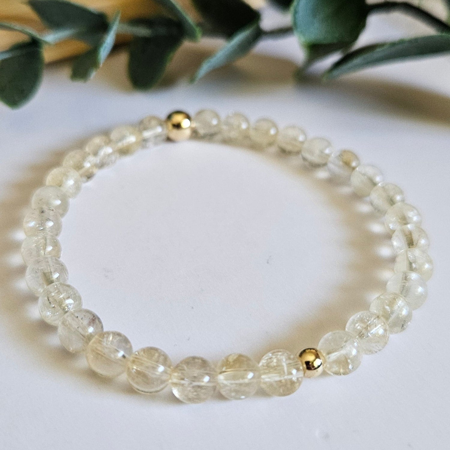 Pearl bracelet on a white surface with green leaves in the background