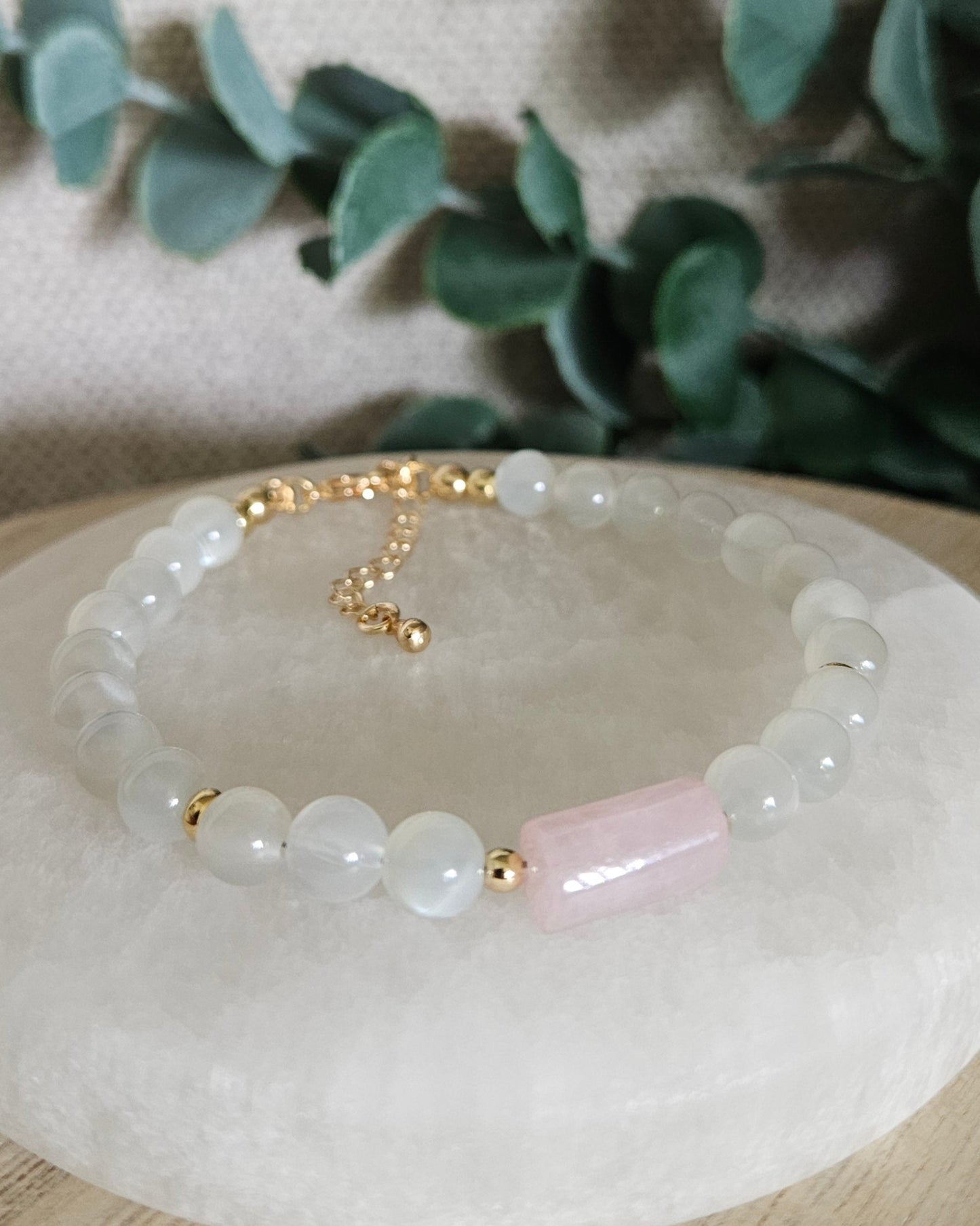 White Moonstone bracelet with a Rose Quartz barrel focal and gold accents displayed on a round selenite plate