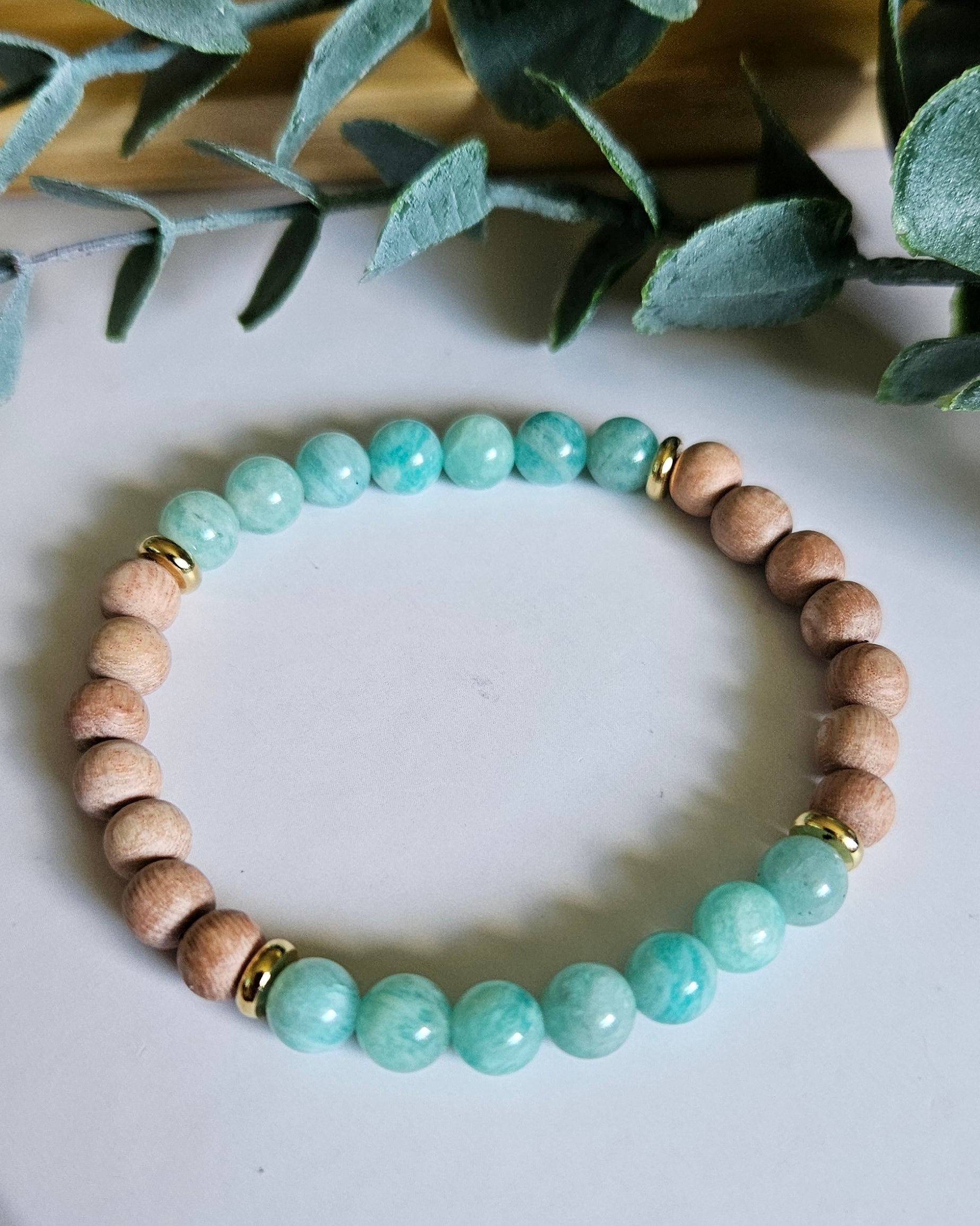 Beaded bracelet with turquoise and beige beads on a white surface with green leaves in the background