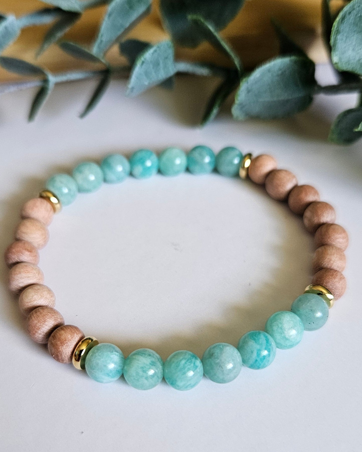 Beaded bracelet with turquoise and beige beads on a white surface with green leaves.