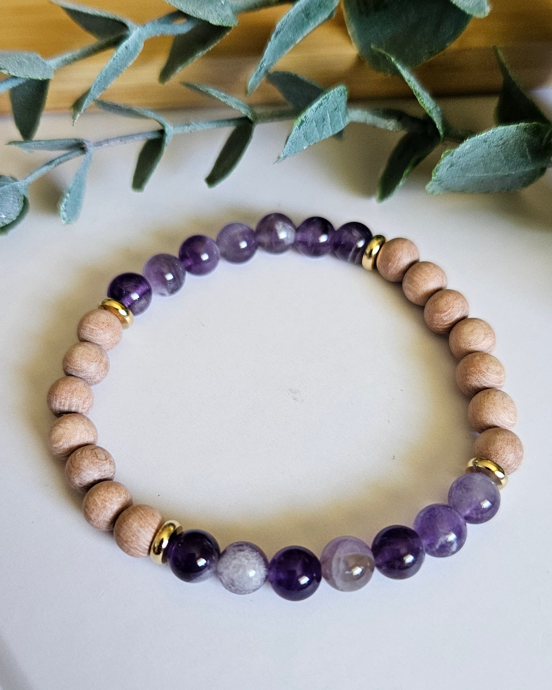 Beaded bracelet with purple and gold accents on a white surface with green leaves in the background