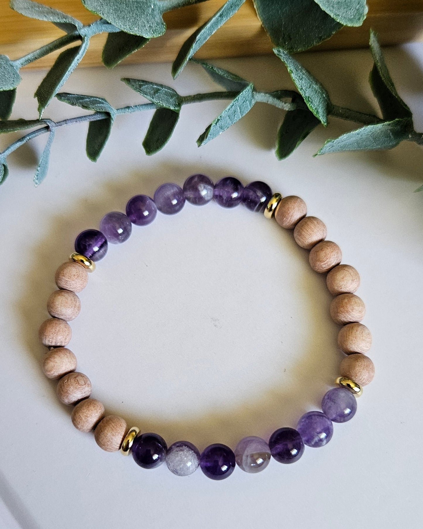 Beaded bracelet with purple and beige beads on a white surface with green leaves.