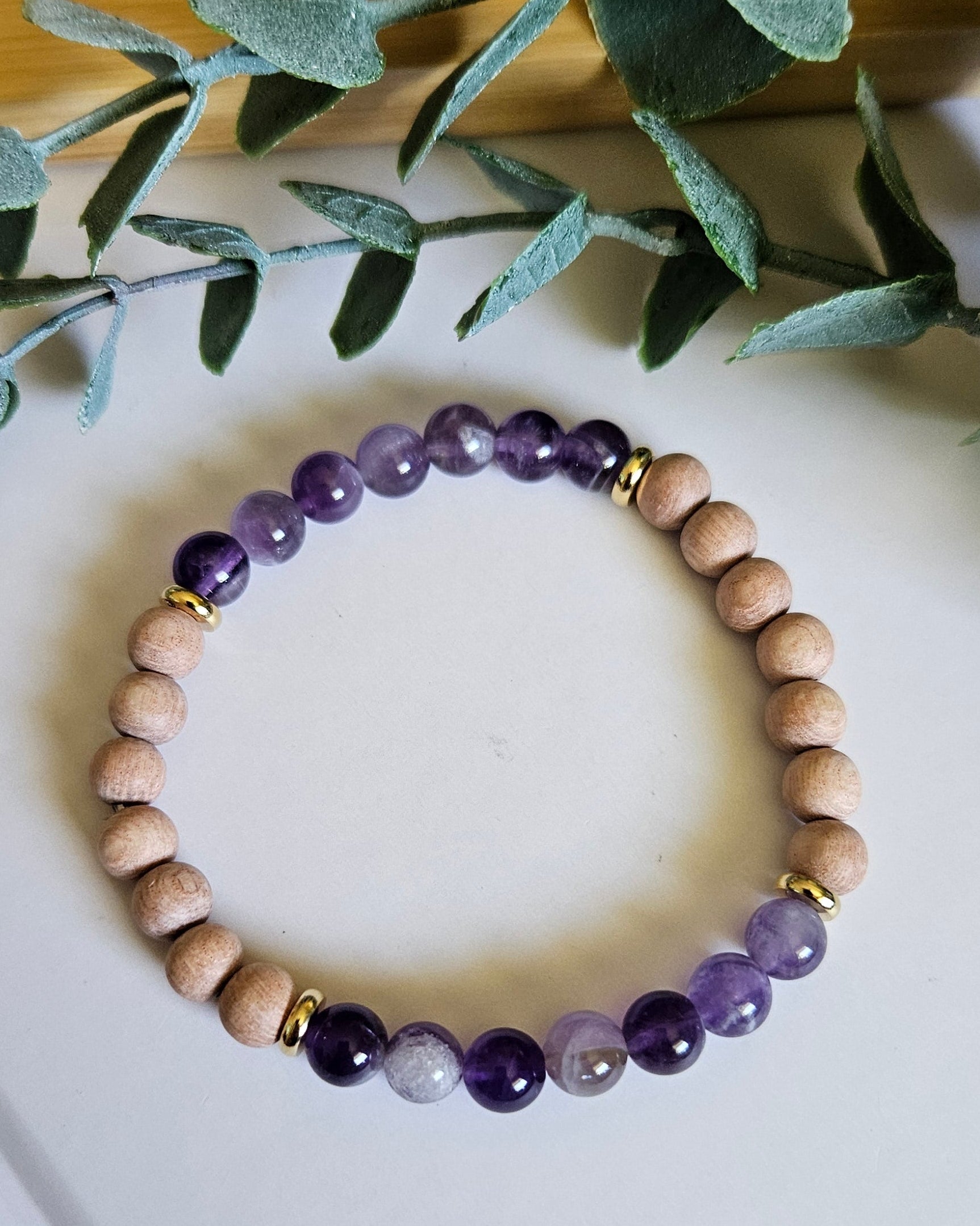 Beaded bracelet with purple and beige beads on a white surface with green leaves.