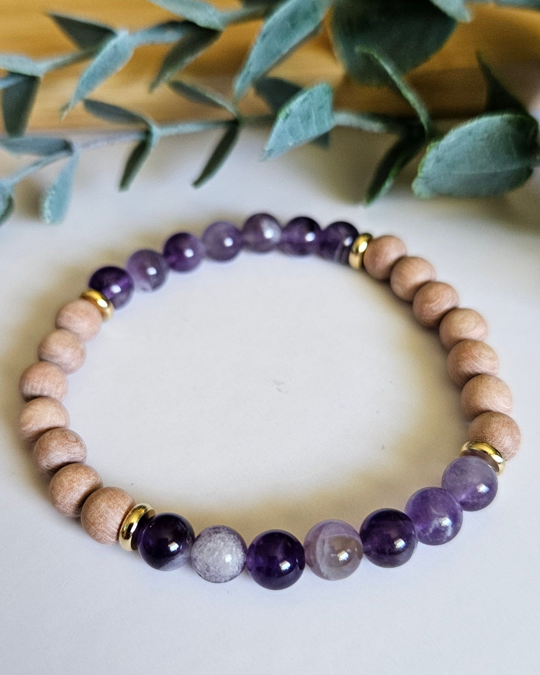 Beaded bracelet with purple and white stones on a white surface with green leaves in the background