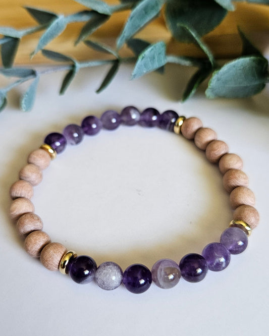 Beaded bracelet with purple and white stones on a white surface with green leaves in the background