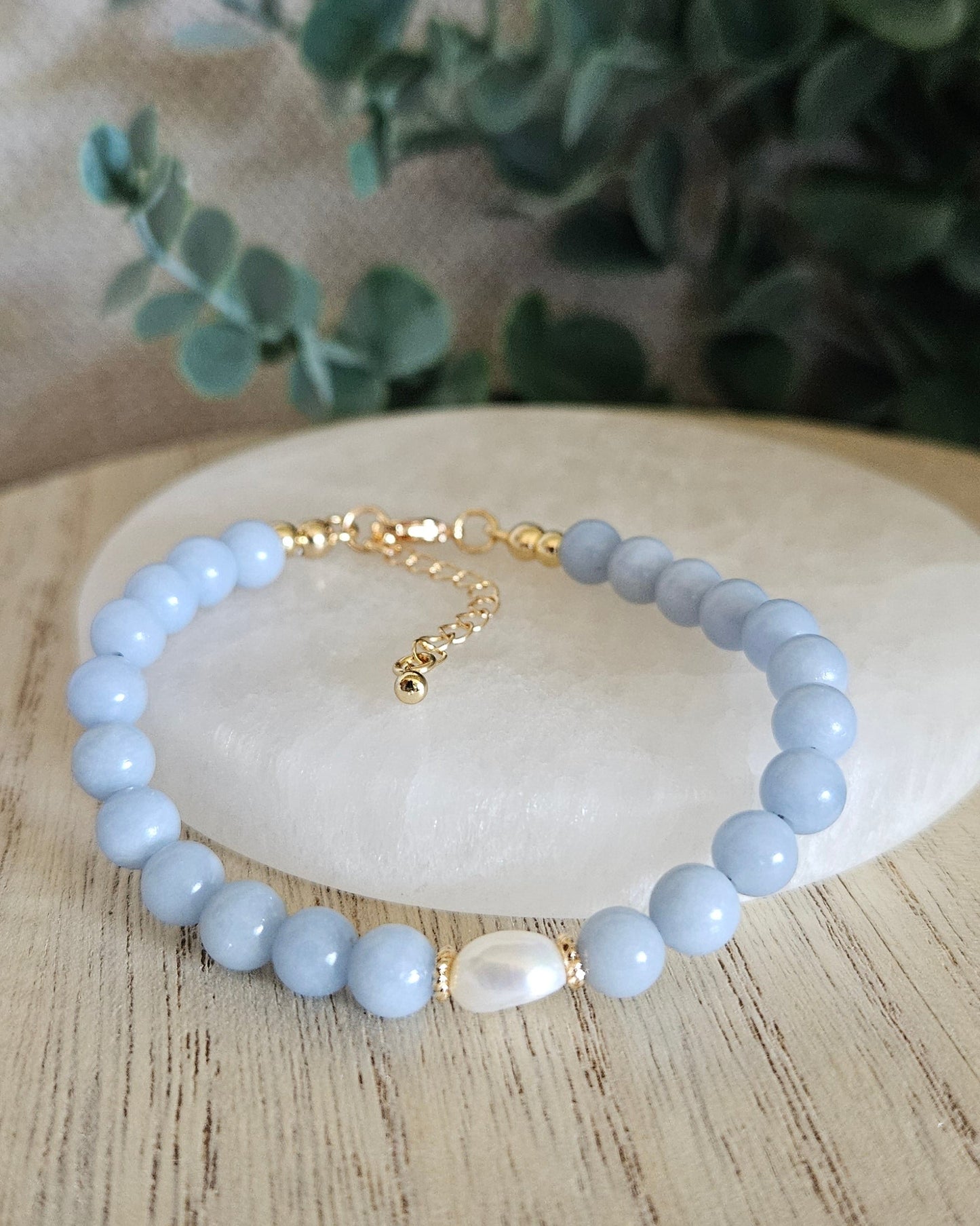 Light blue beaded bracelet with gold accents on a wooden surface with greenery.