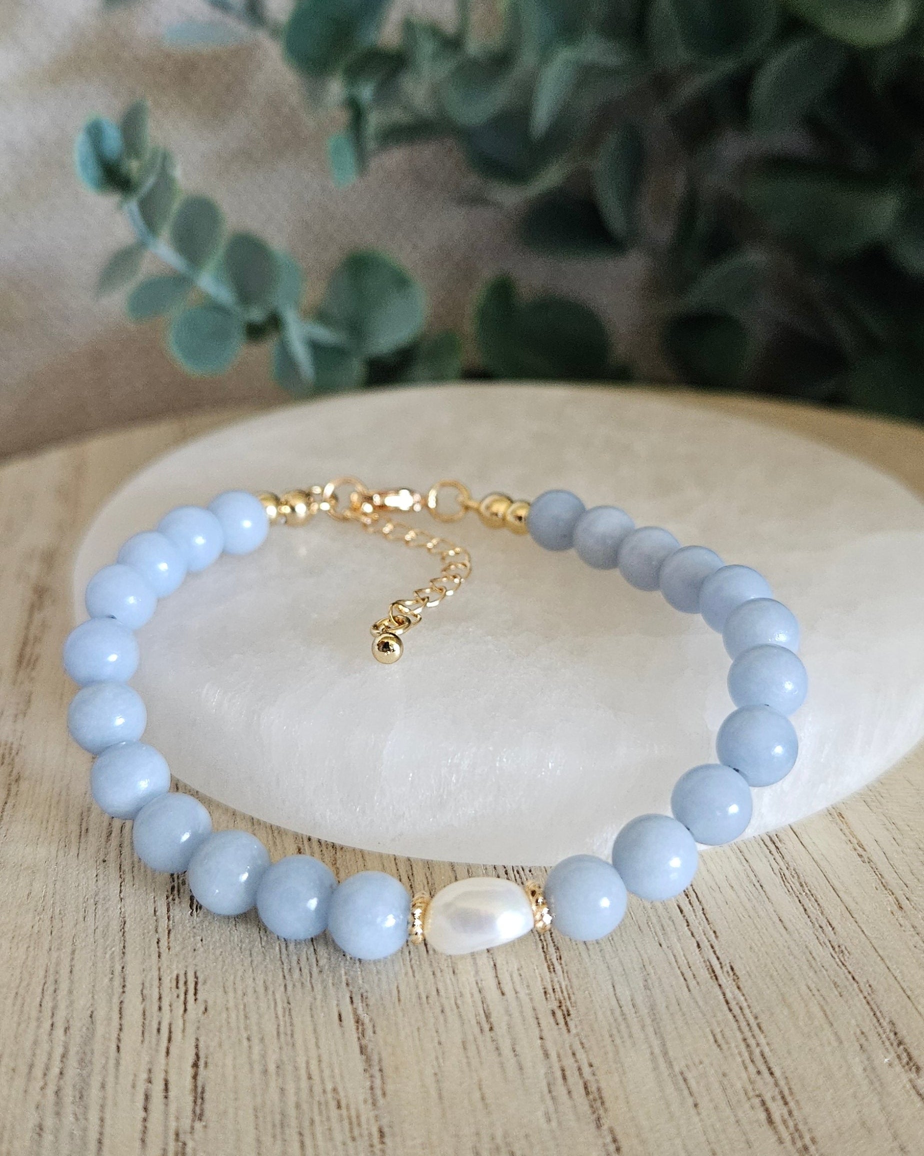 Light blue beaded bracelet with gold accents on a wooden surface with greenery.