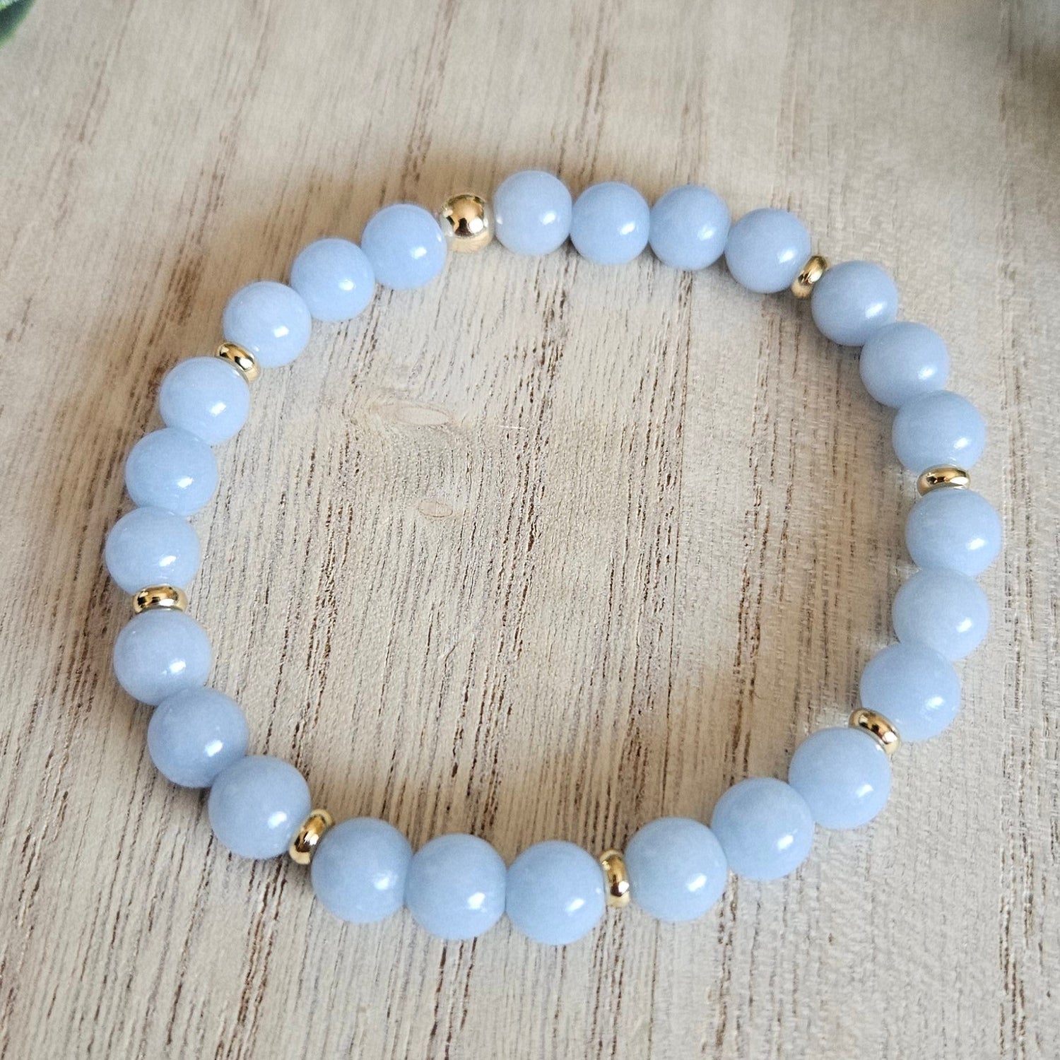 Light blue beaded bracelet with gold accents on a wooden surface with a leafy branch.
