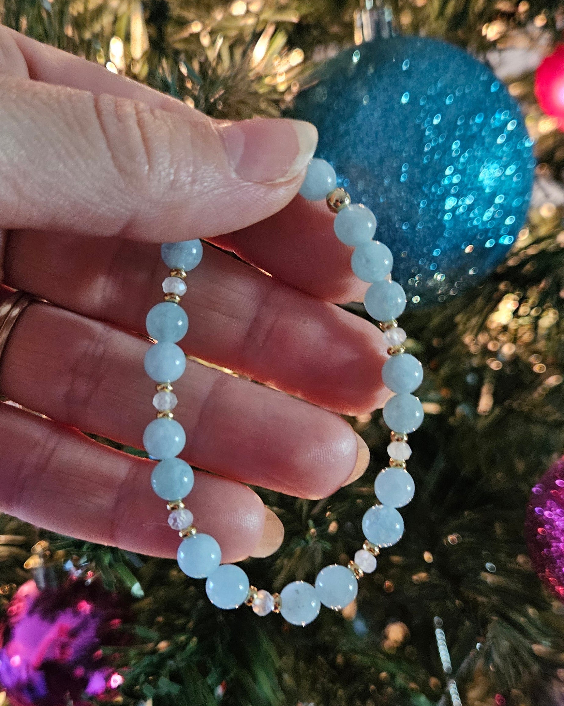 Hand holding a beaded bracelet with Christmas decorations in the background