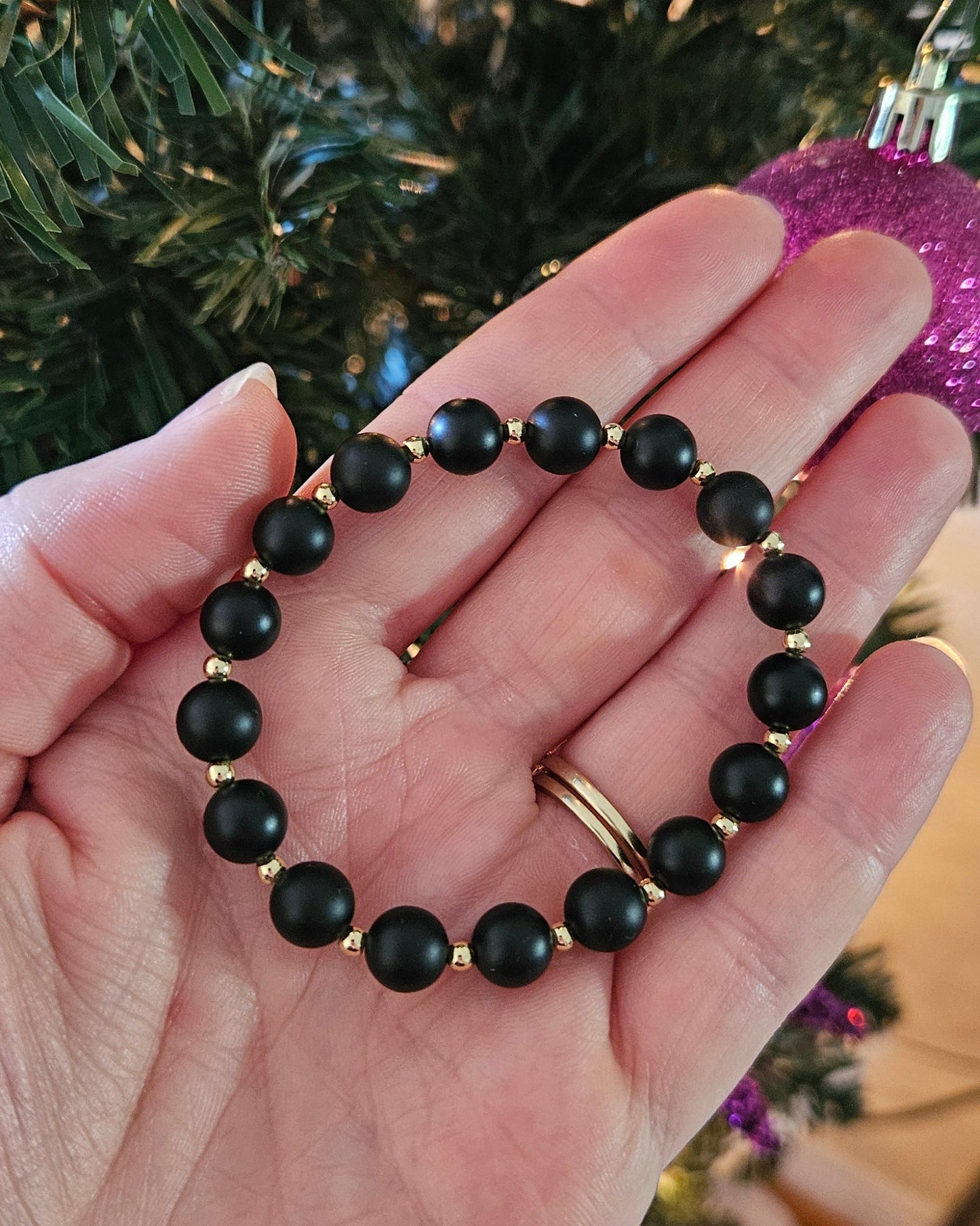 Hand holding a black beaded bracelet with Christmas decorations in the background
