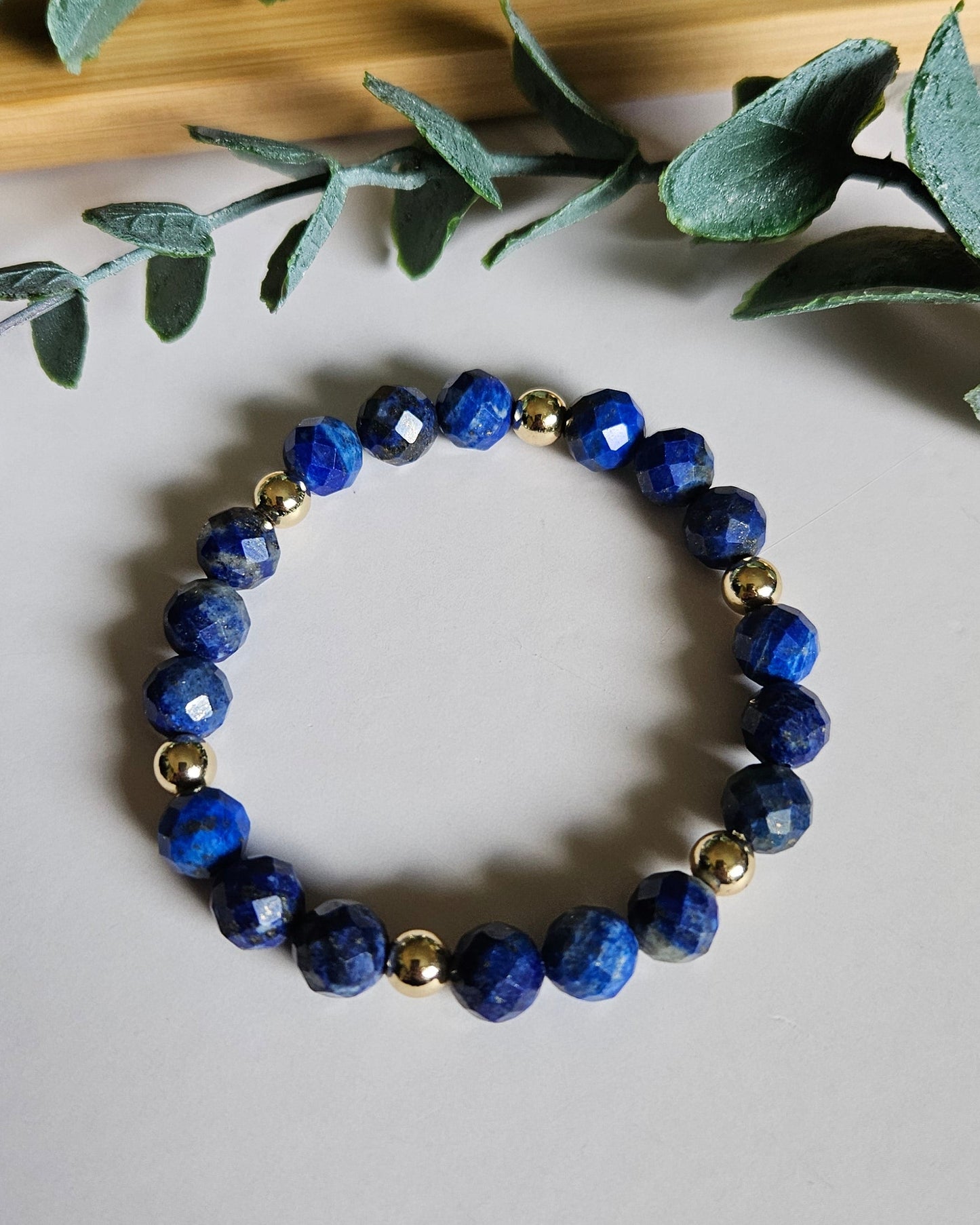 Blue beaded bracelet on a white surface with green leaves in the background