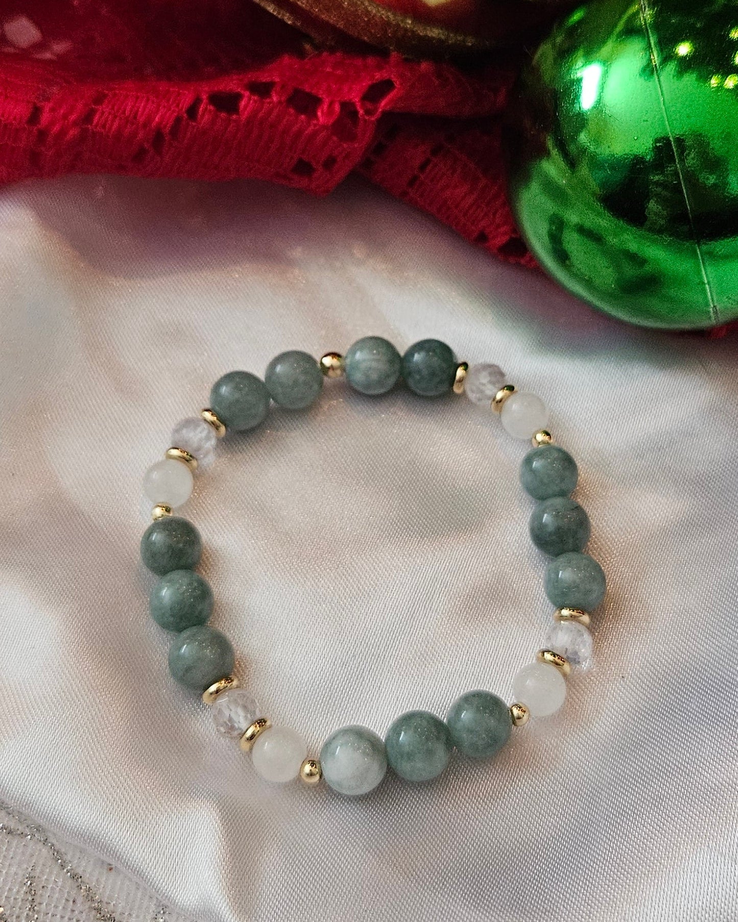 Green beaded bracelet on a textured fabric background with Christmas decorations.