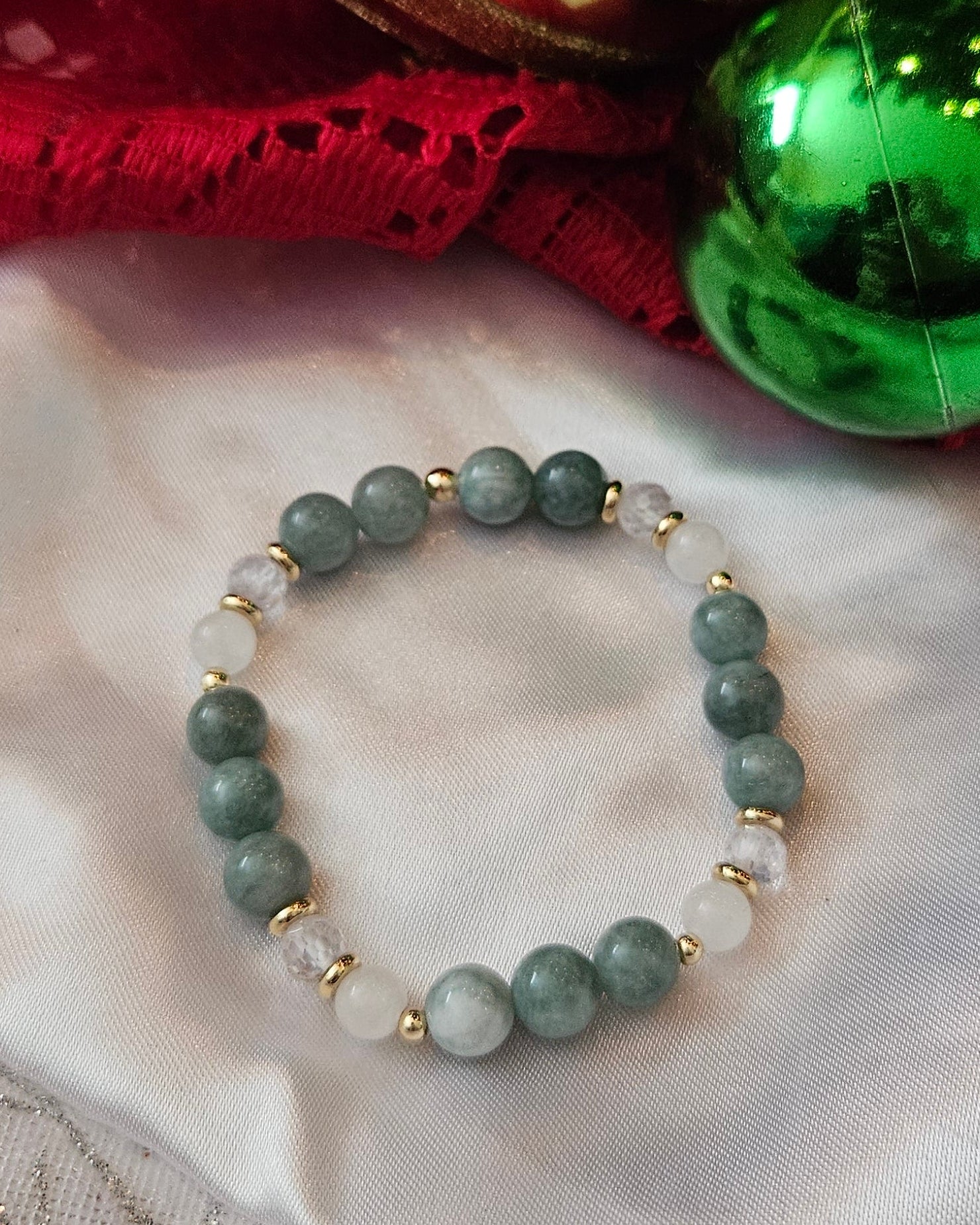 Green beaded bracelet on a textured fabric background with Christmas decorations.