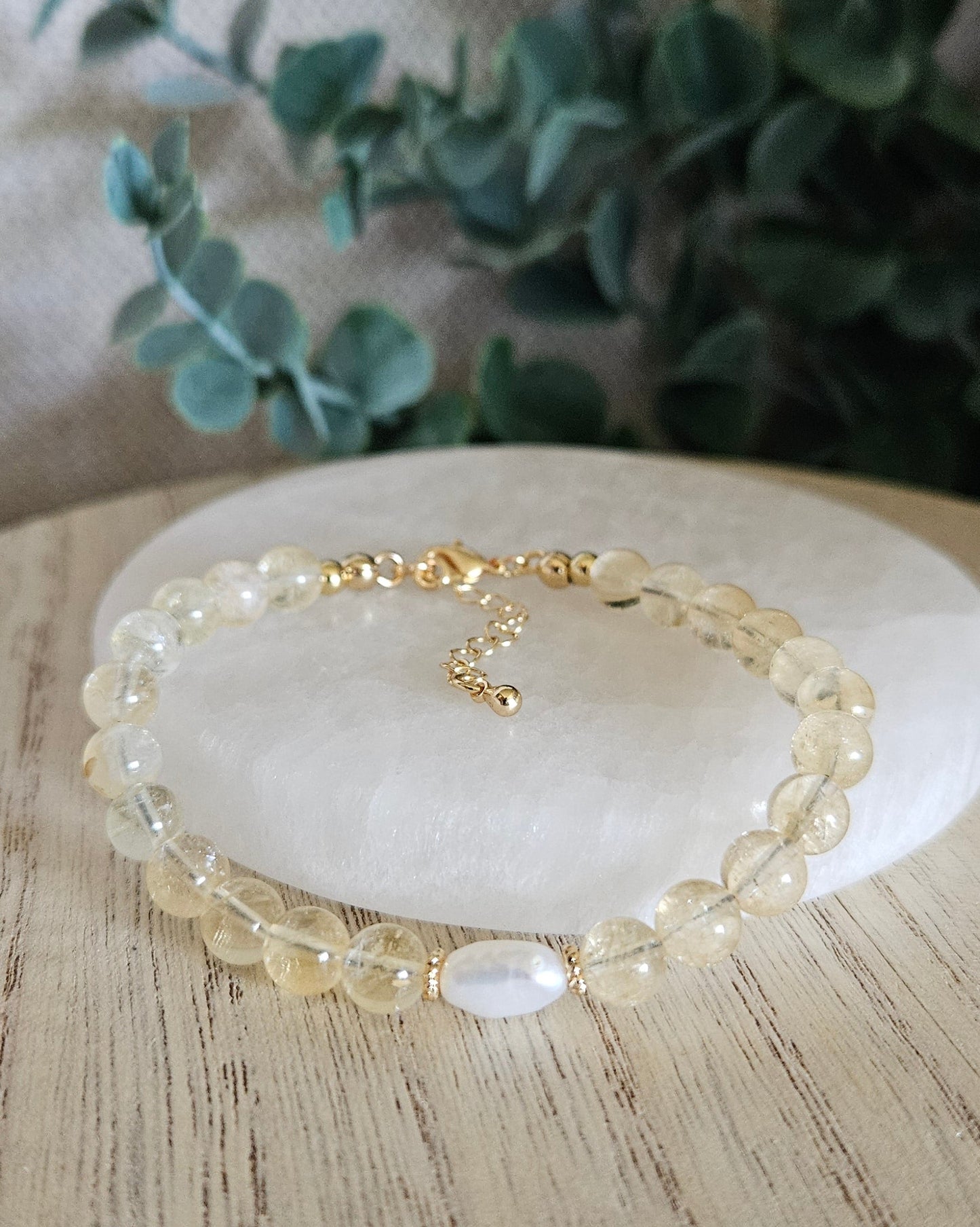 yellow citrine bracelet with freshwater pearl on selenite plate with greenery in the background
