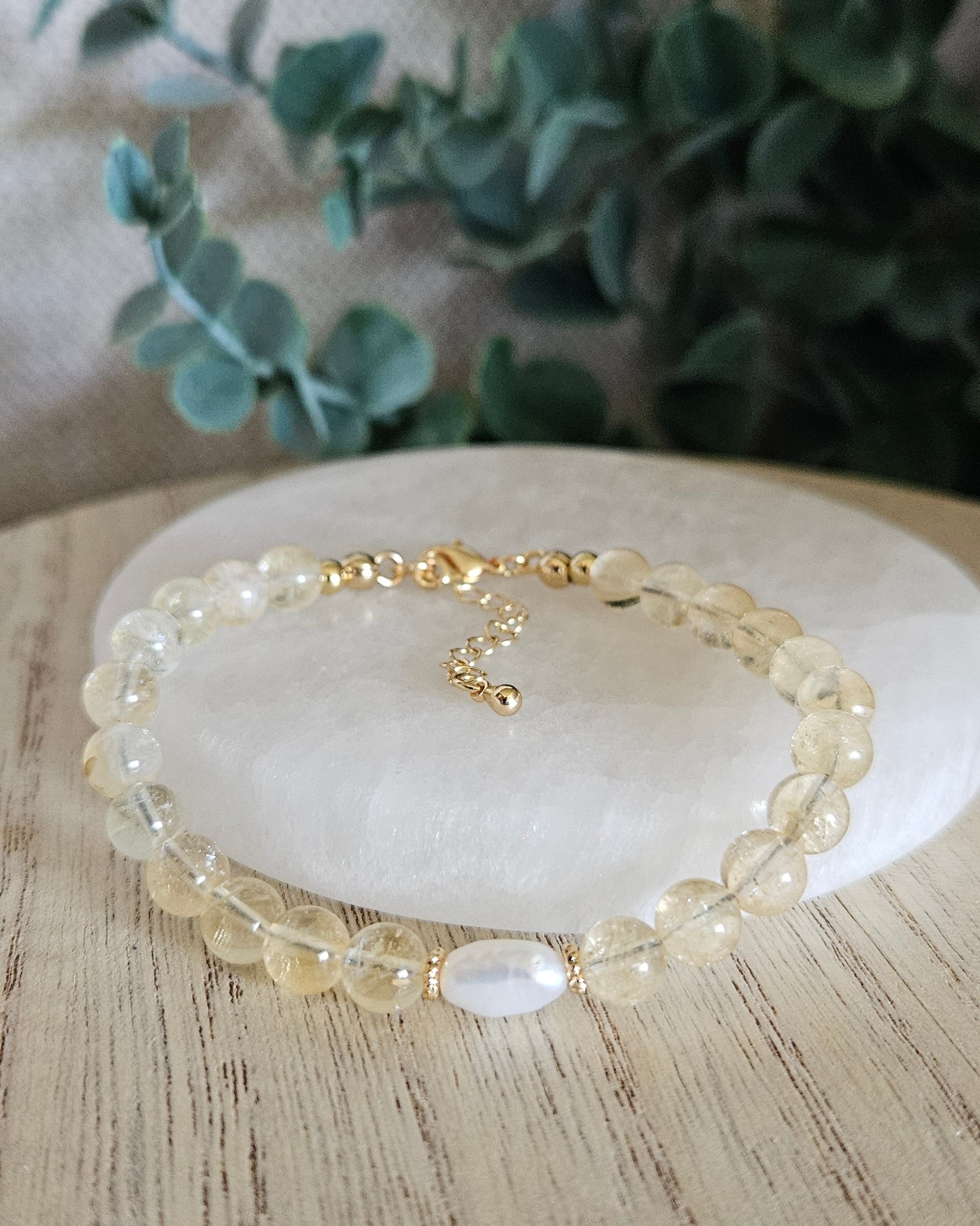 yellow citrine bracelet with freshwater pearl on selenite plate with greenery in the background