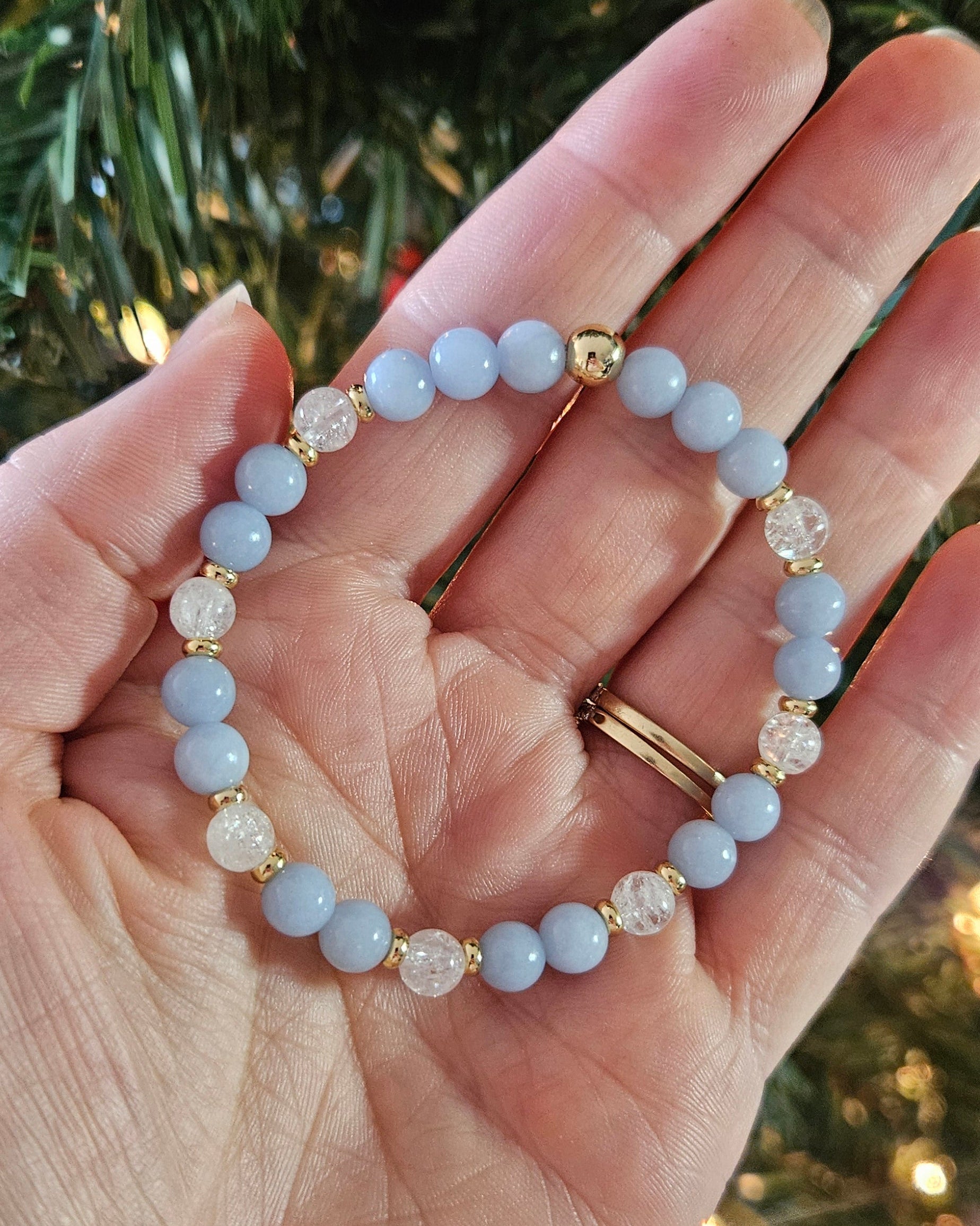 Hand holding two beaded bracelets with a Christmas tree background