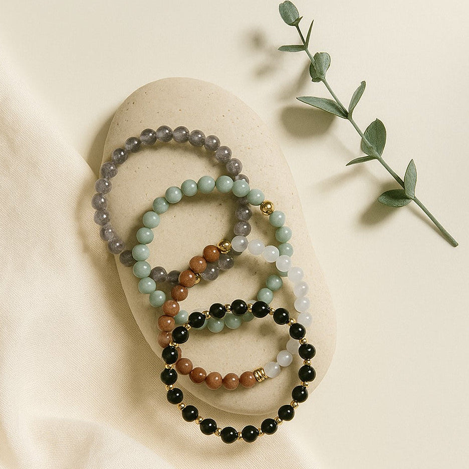 Set of three beaded bracelets on a beige fabric surface with a leafy branch.