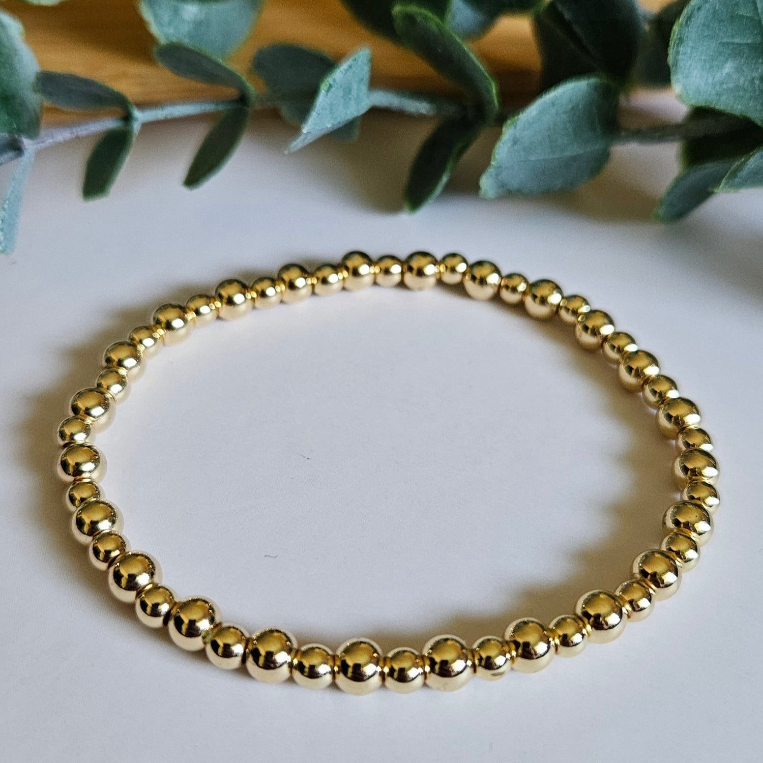 Gold bracelet on a white surface with green leaves
