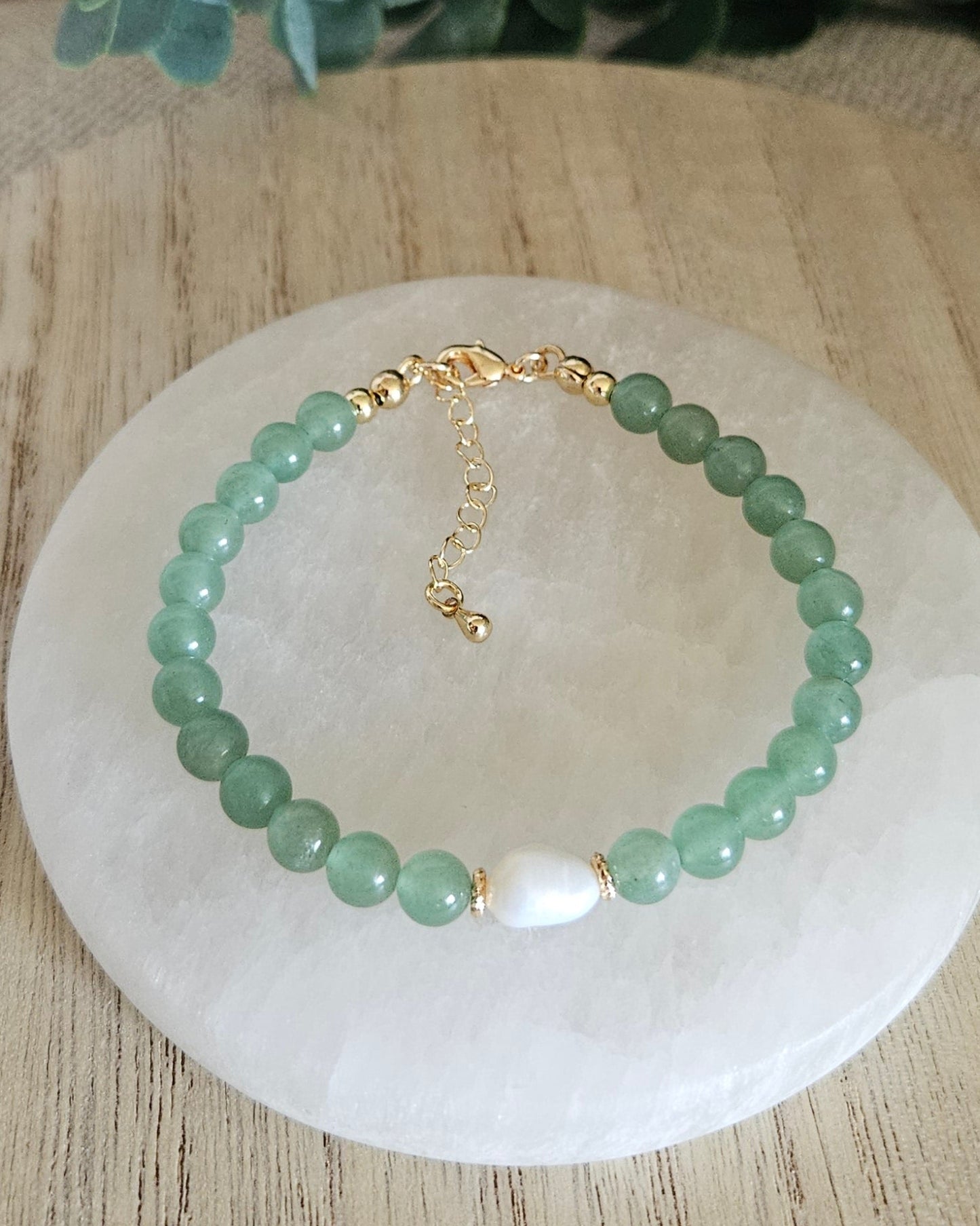 Green aventurine bracelet on a selenite plate with eucalyptus leaves on a wooden surface