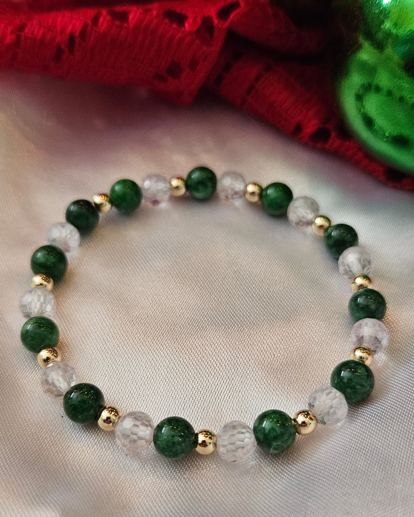 Green beaded bracelet with gold accents on a white fabric background