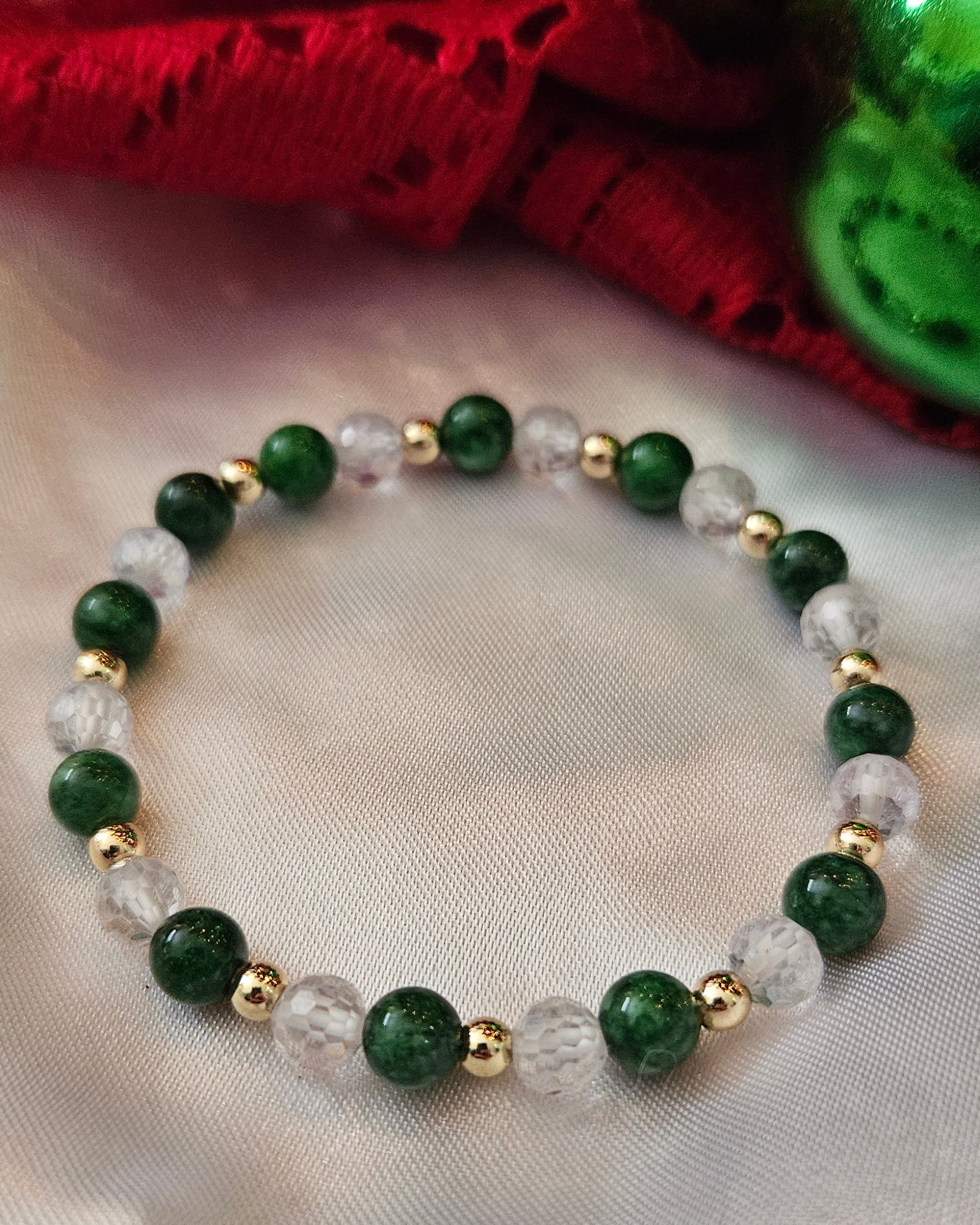 Green beaded bracelet with gold accents on a white fabric background