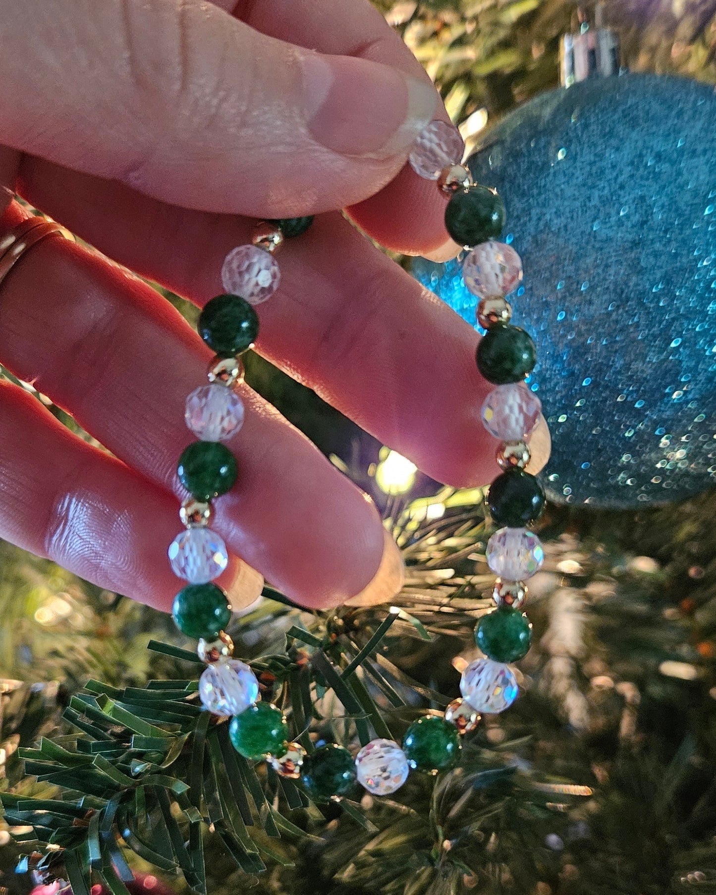 Hand holding a beaded bracelet with green, white, and clear beads against a festive background.