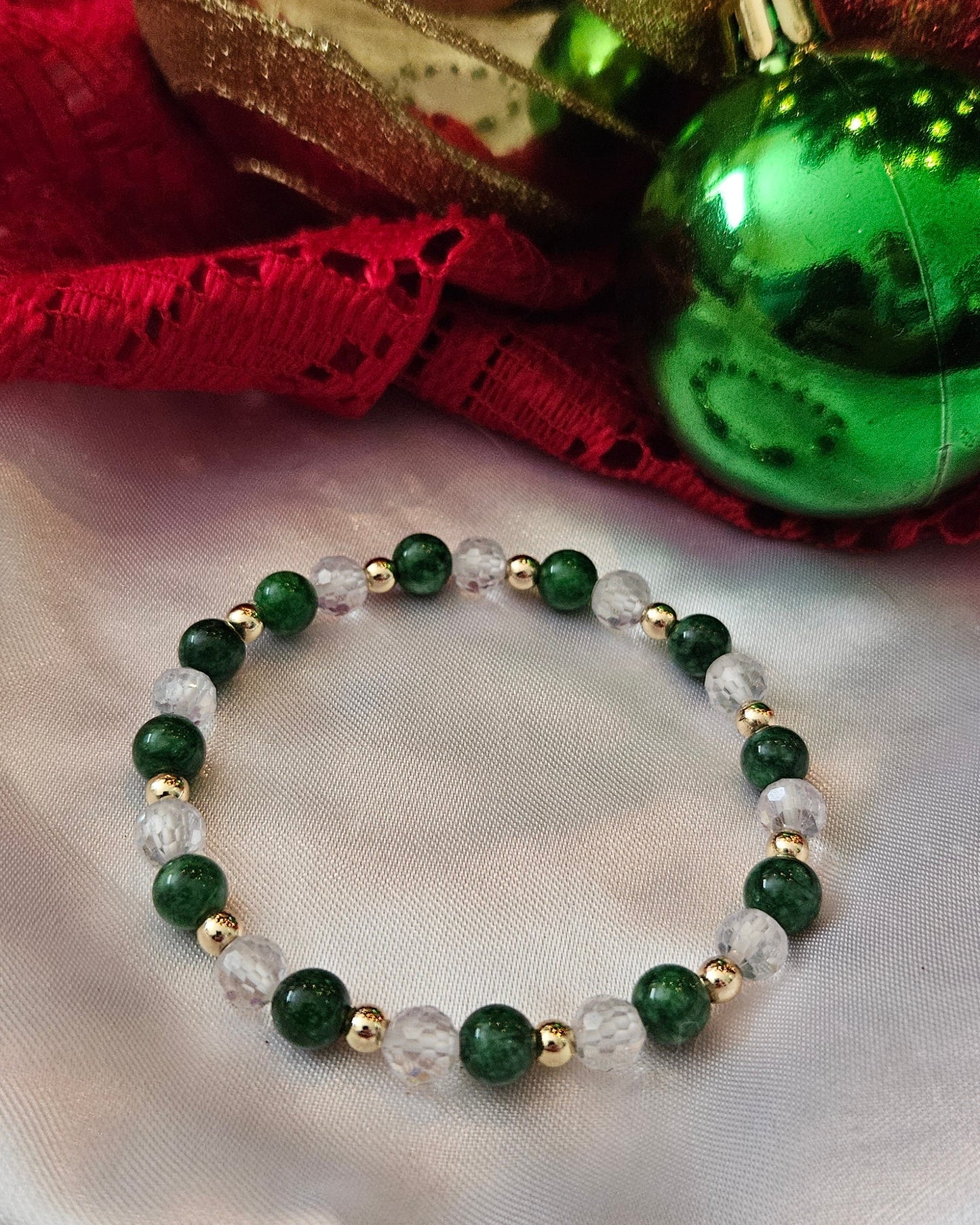 Green and gold beaded bracelet on a white fabric background with Christmas ornaments.