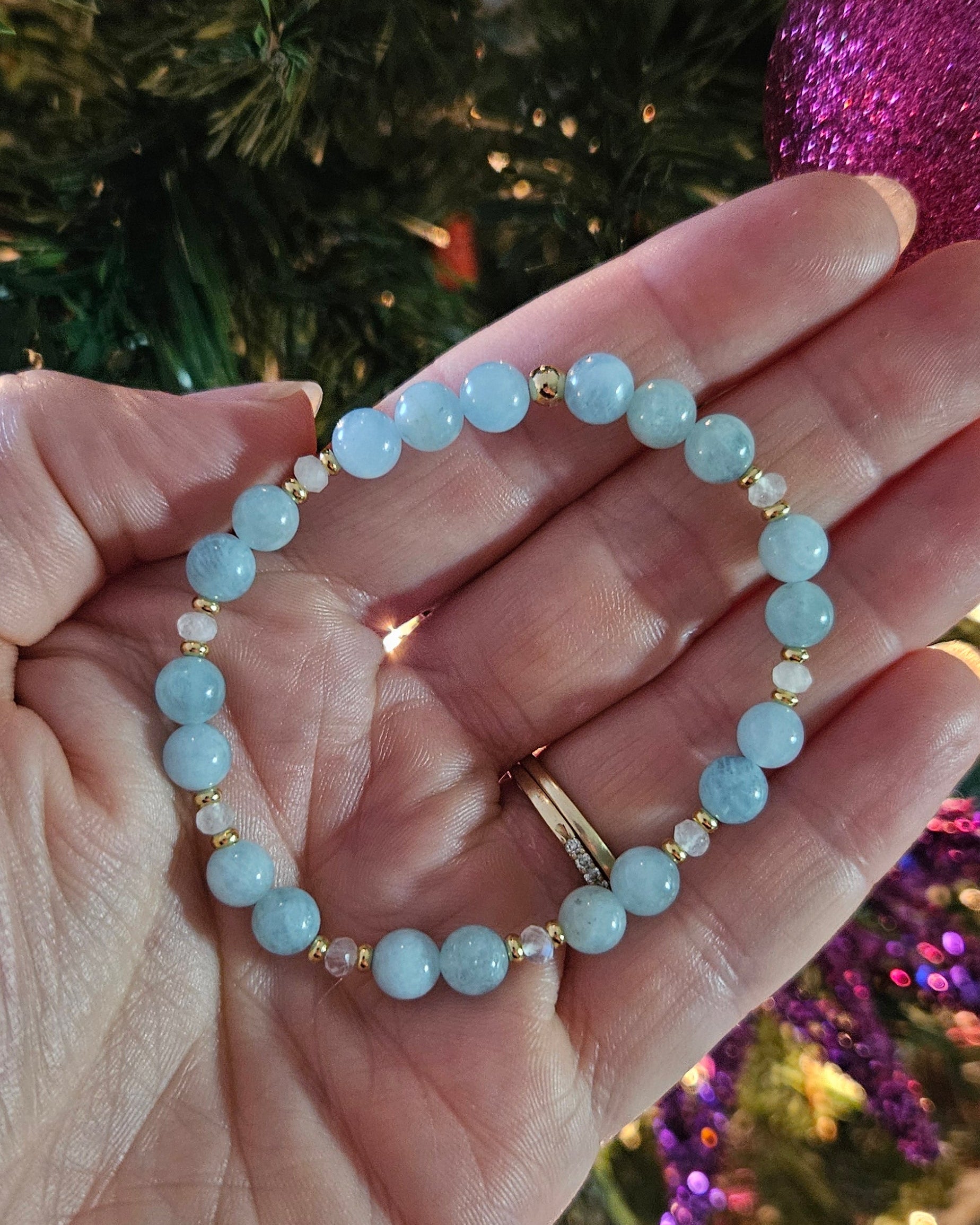 Hand holding a beaded bracelet with a Christmas tree in the background