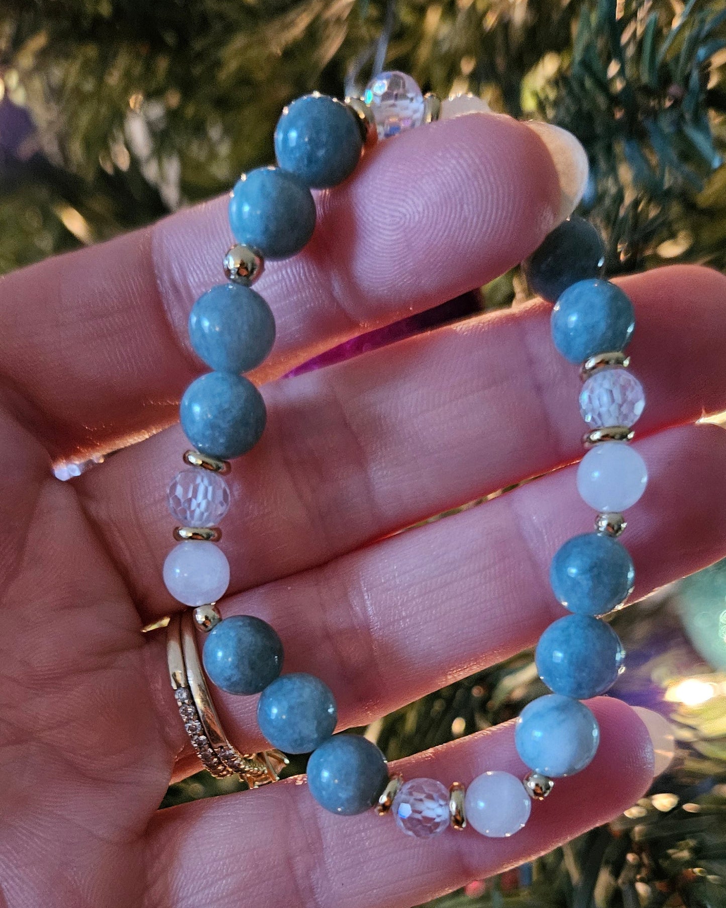Hand holding a blue beaded bracelet with a Christmas tree in the background