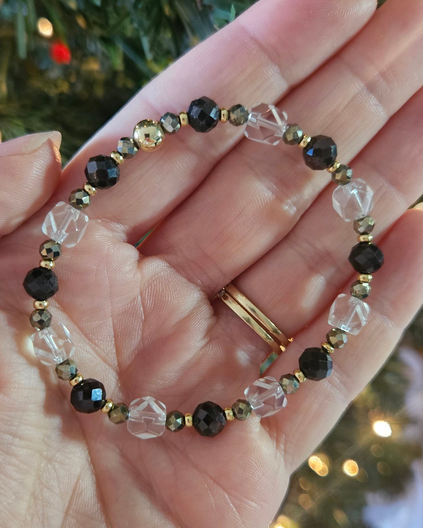 Hand holding a beaded bracelet with a blurred Christmas tree background