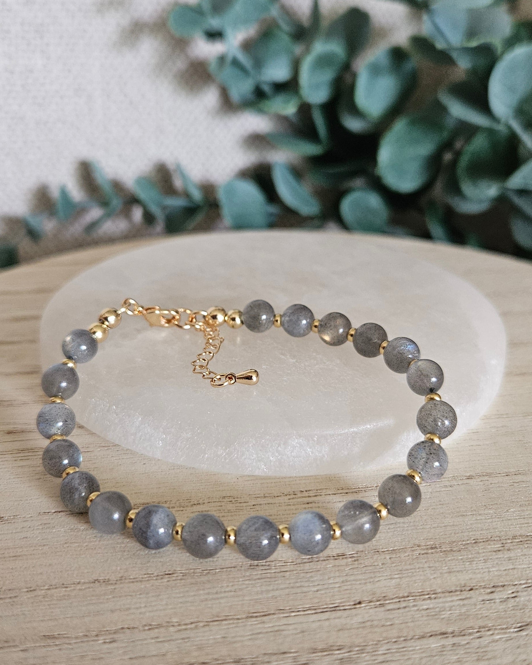 labradorite bracelet on selenite plate and greenery in the background