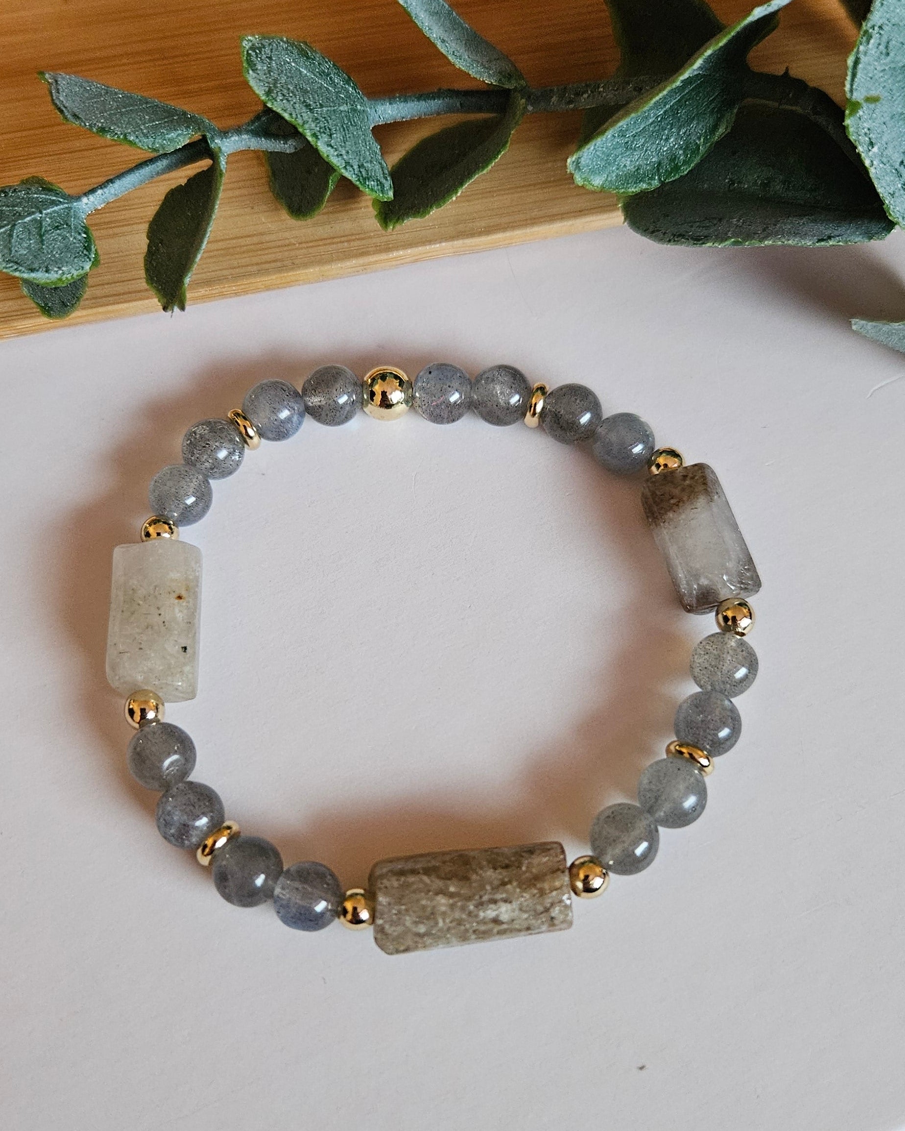 Bracelet with gray beads on a white surface with green leaves