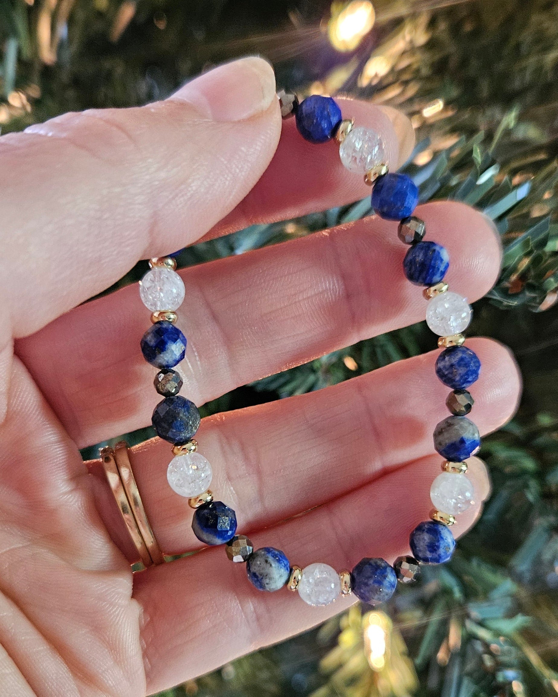 Hand holding a beaded bracelet with a blurred Christmas tree background