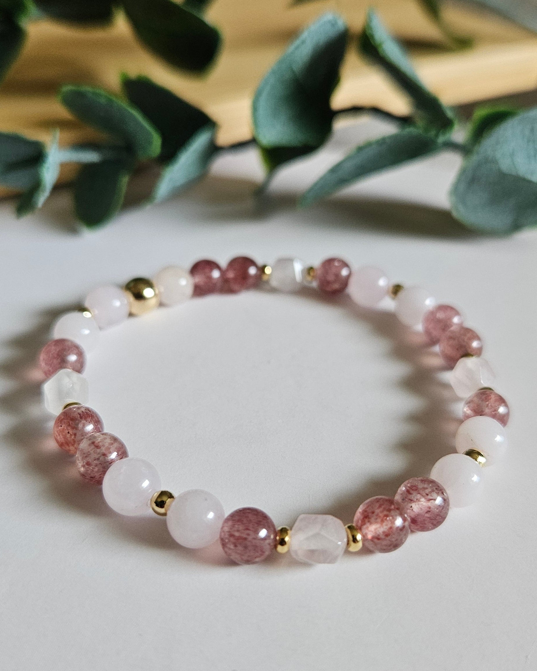 Beaded bracelet with pink and gold accents on a white surface with greenery in the background