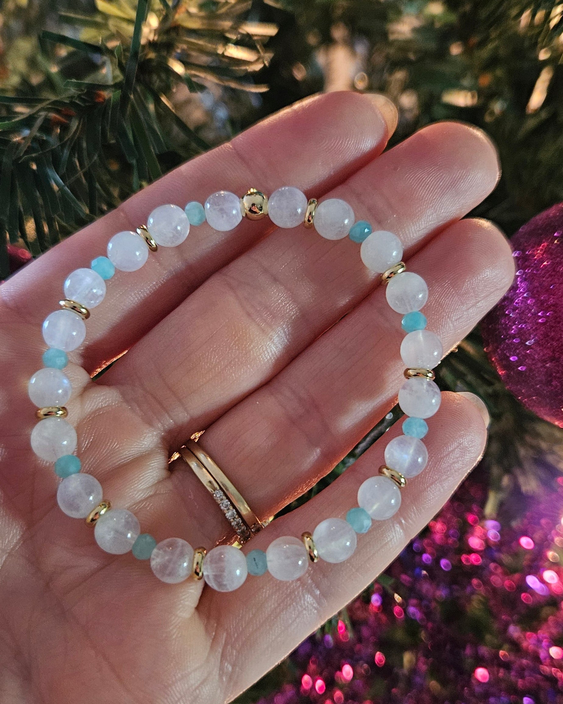 Hand wearing a beaded bracelet with a Christmas tree in the background