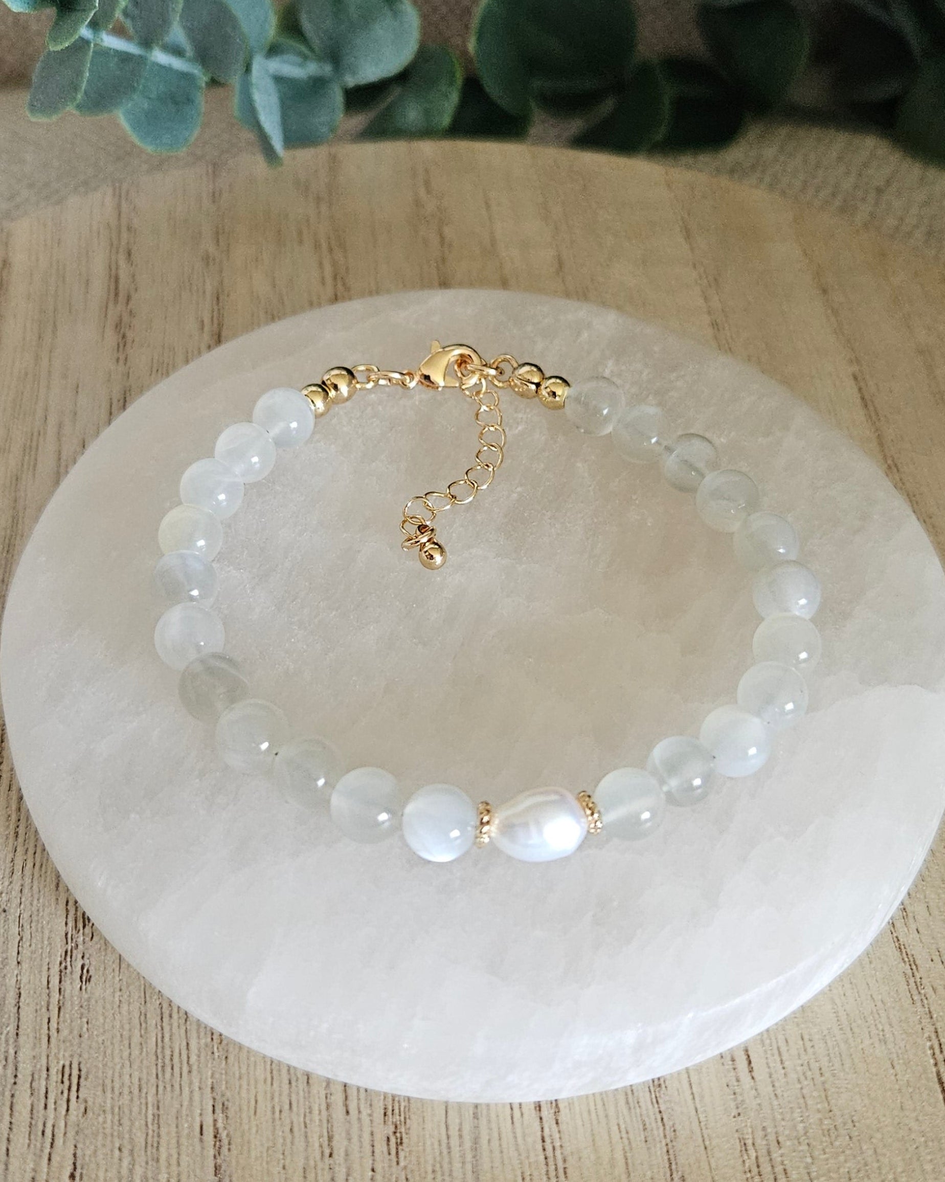 moonstone bracelet with freshwater pearl focal on a selenite plate with greenery in background