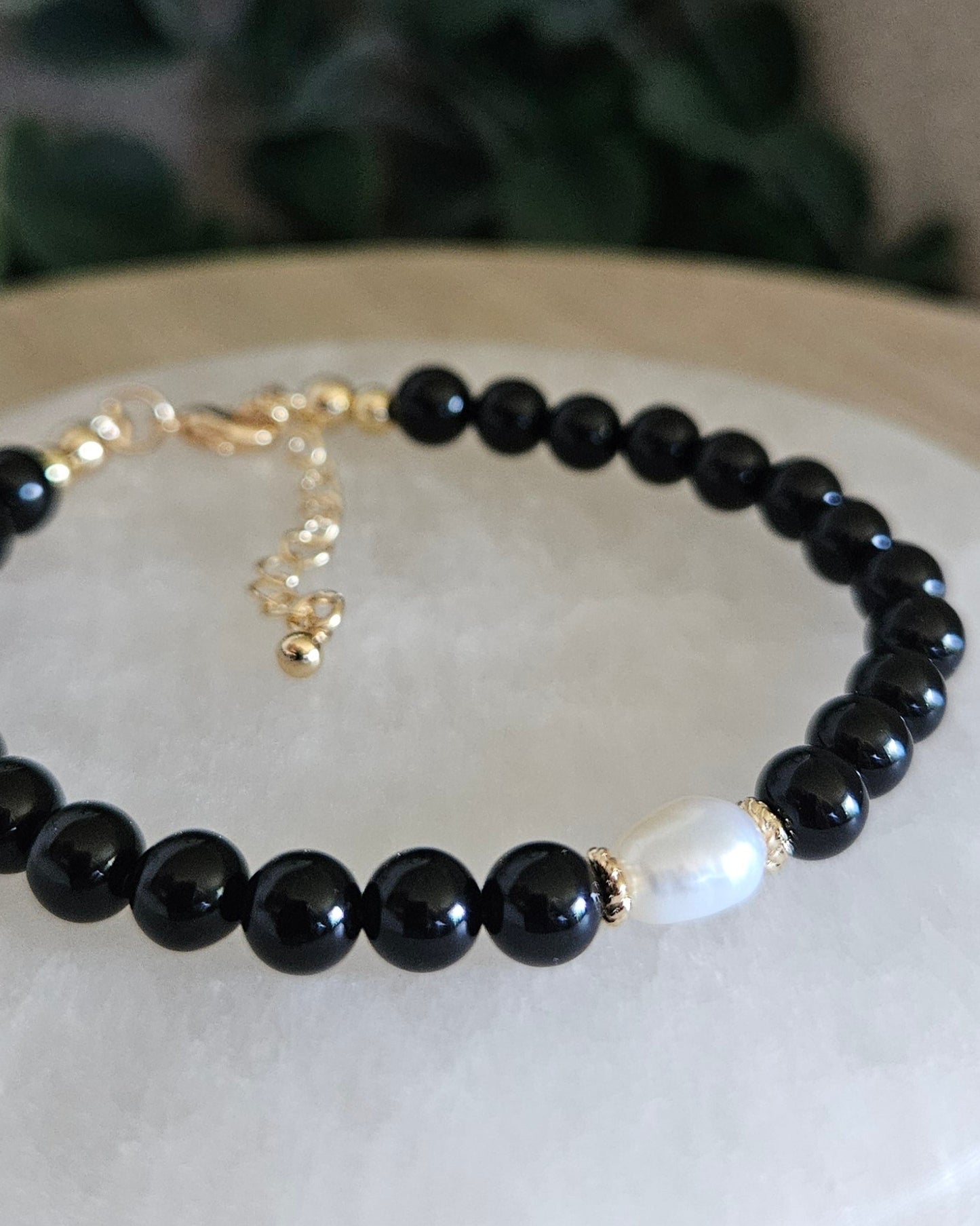Black beaded bracelet with a gold clasp on a white stone surface with greenery in the background