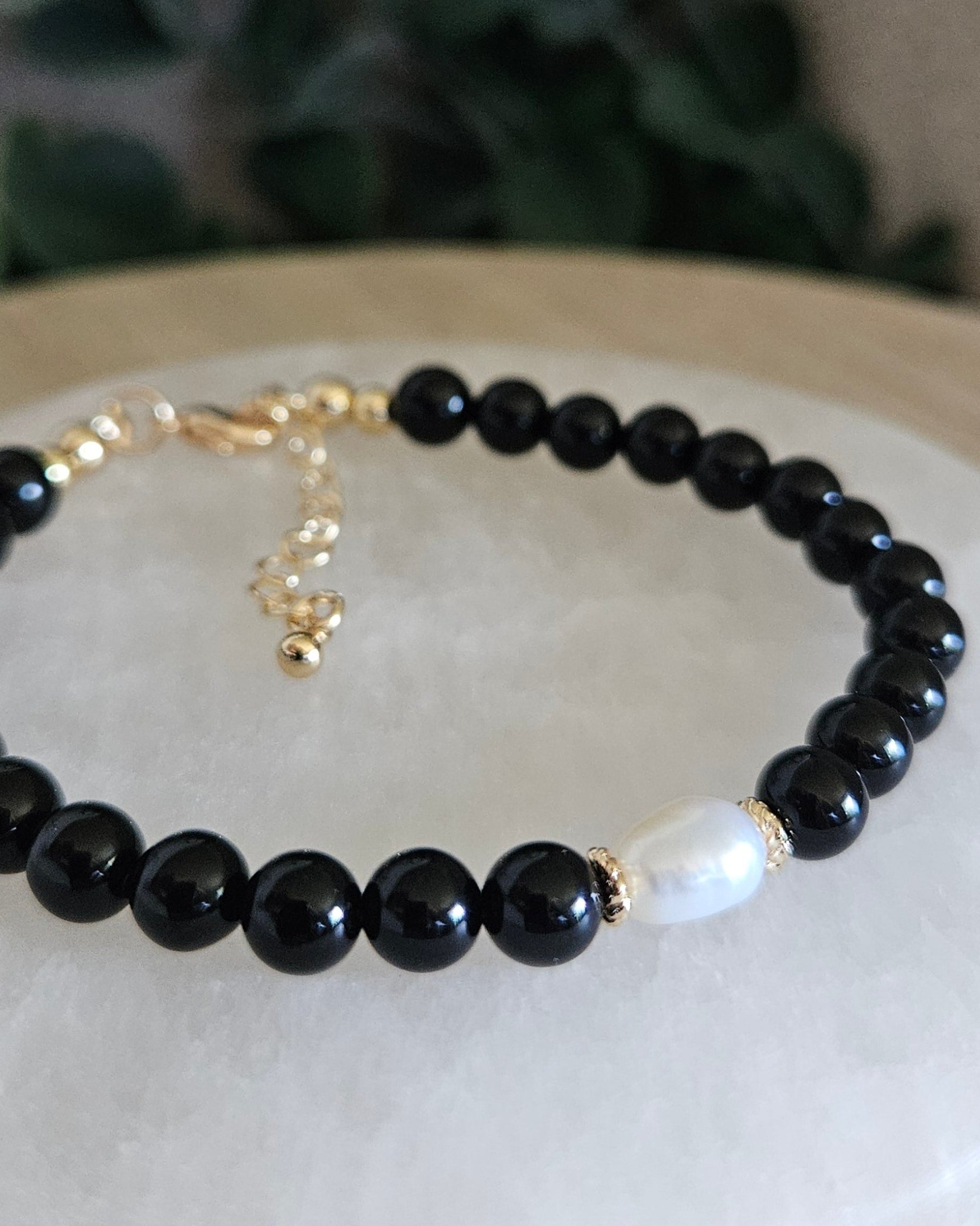 Black beaded bracelet with a gold clasp on a white stone surface with greenery in the background