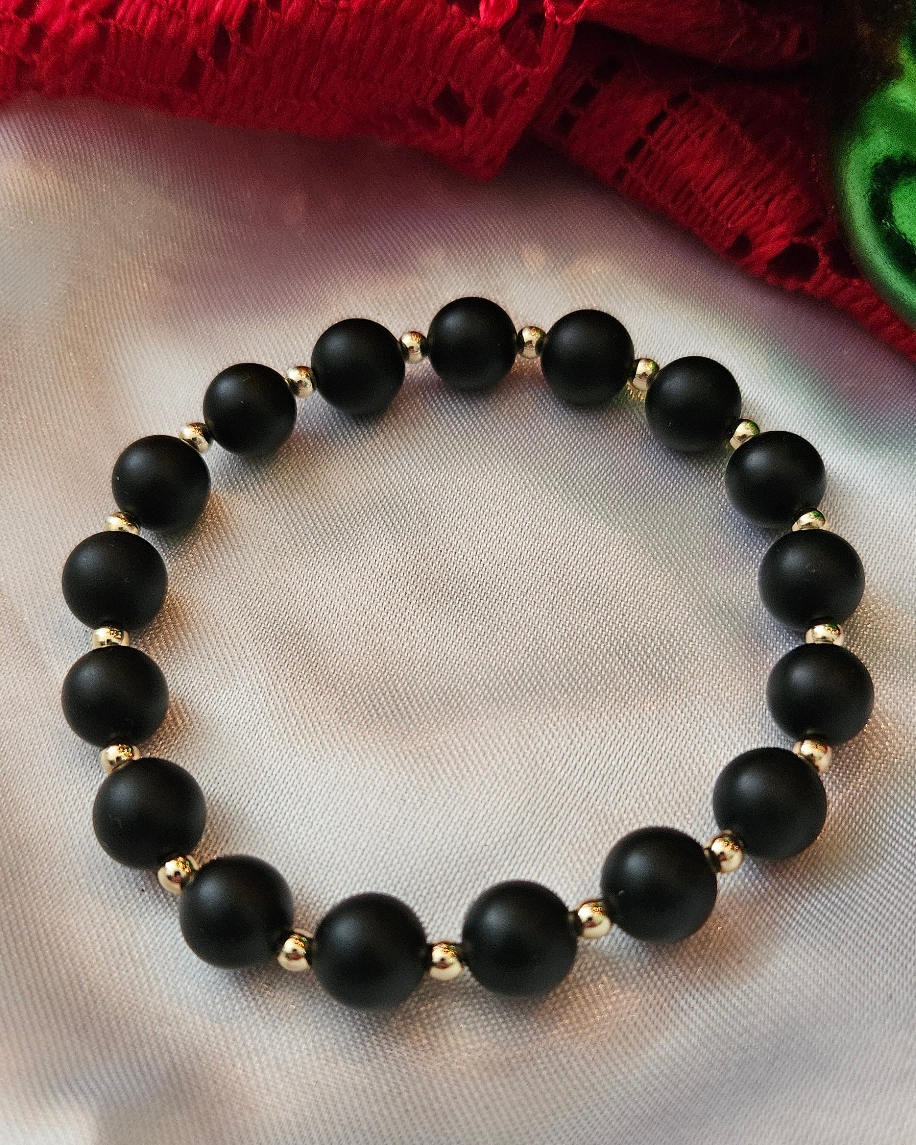 Black beaded bracelet on a white surface with a red fabric background