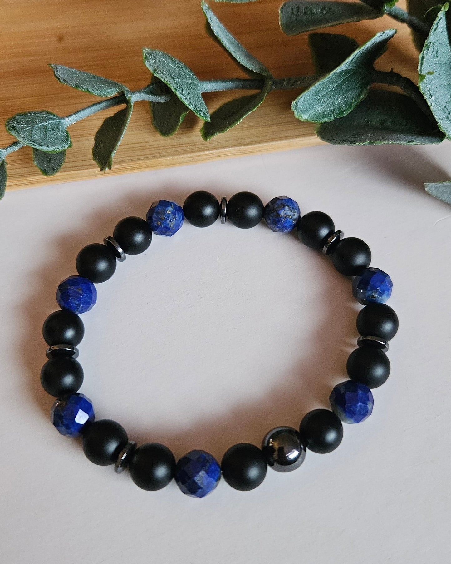 Black and blue beaded bracelet on a white surface with green leaves.