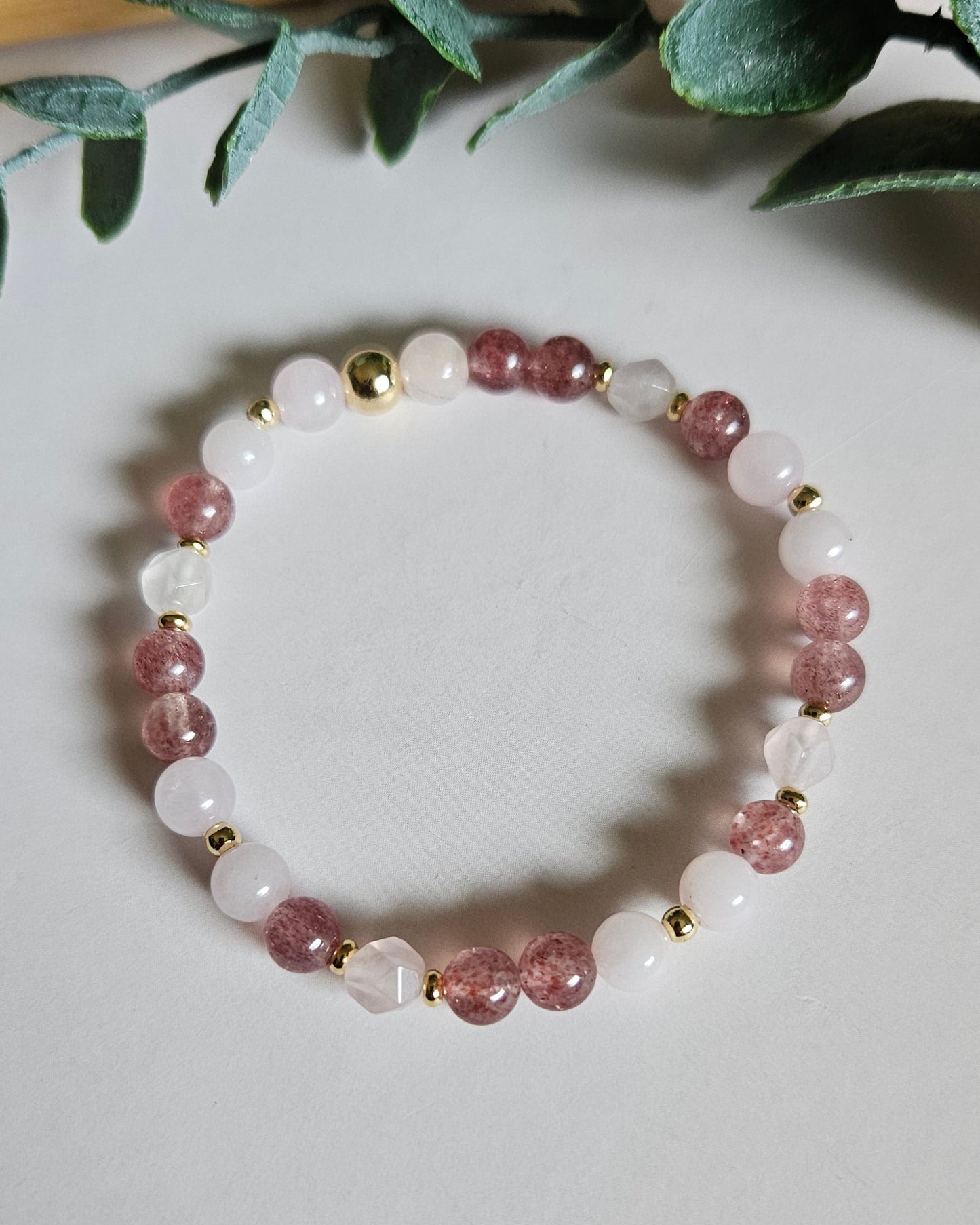 Pink beaded bracelet on a white surface with green leaves in the background