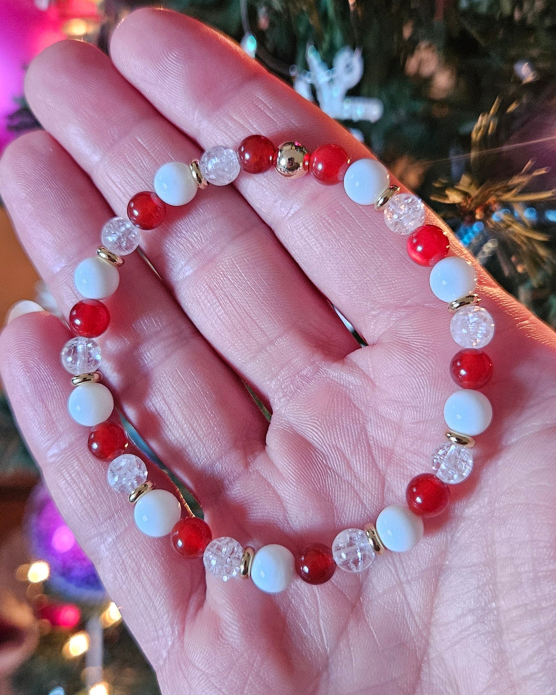 Hand wearing a beaded bracelet with a Christmas tree and lights in the background