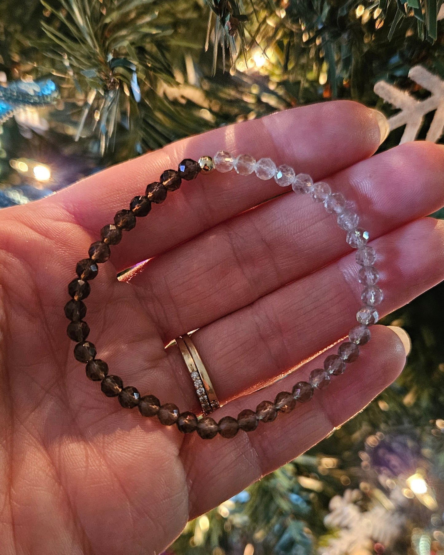 Hand holding a beaded bracelet with a Christmas tree in the background