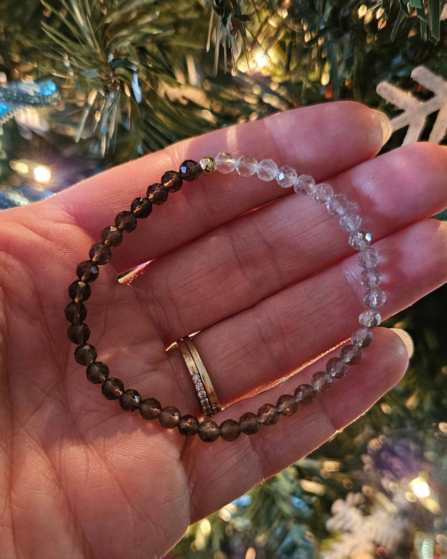 Hand holding a beaded bracelet with a Christmas tree in the background