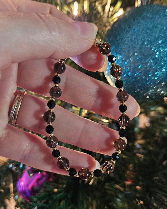 Hand holding a black beaded bracelet with a Christmas tree in the background