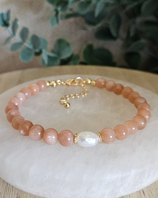 orange beaded bracelet with pearl on selenite plate with greenery in the background