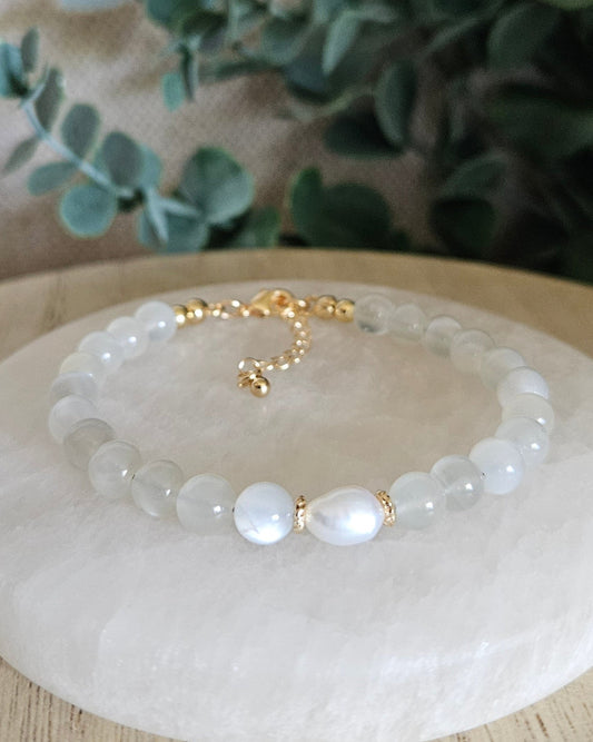 Bracelet with white beads and gold accents on a white stone surface with greenery in the background